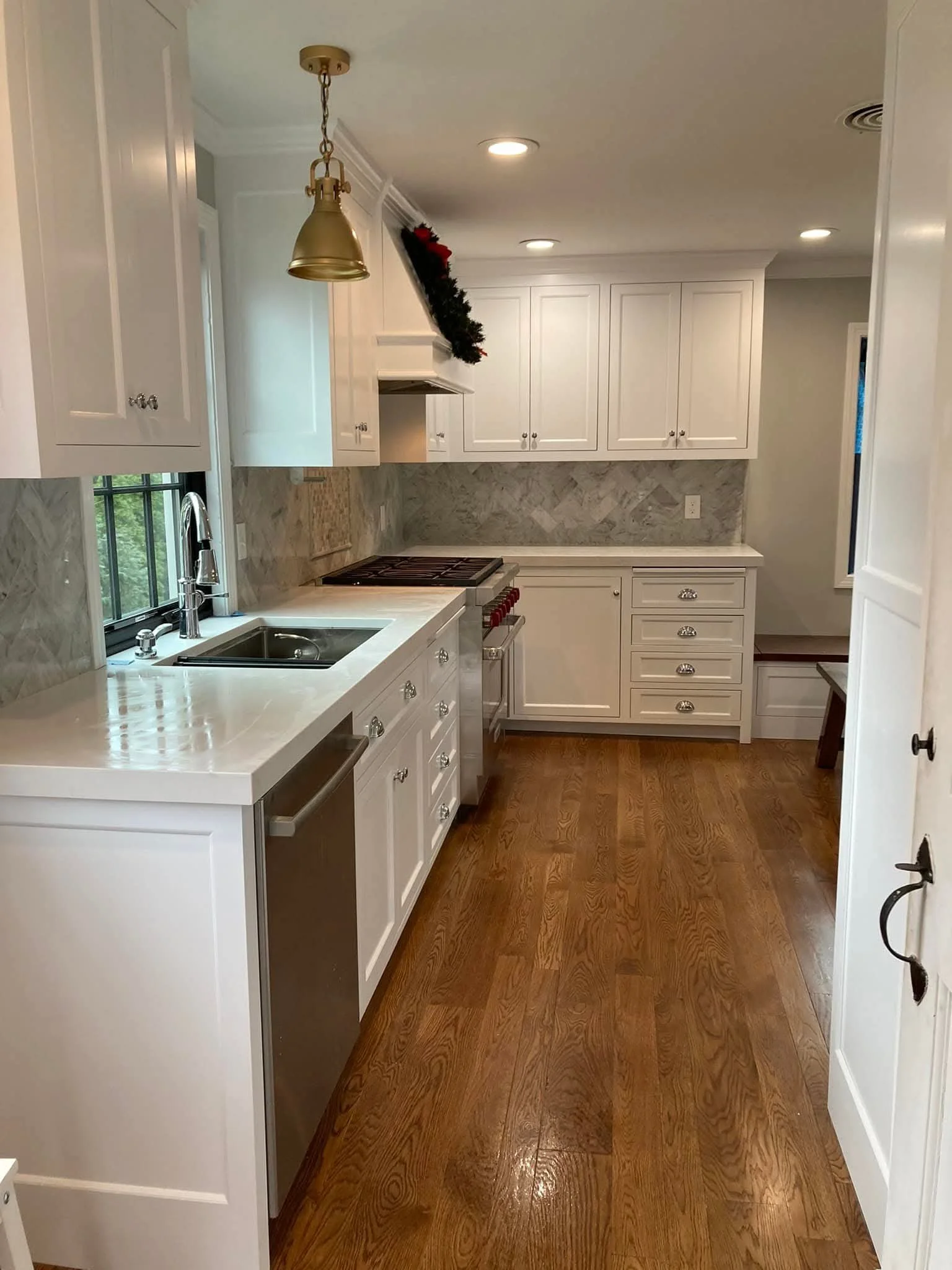 A kitchen with white cabinets, marble backsplash, hardwood floor, and a window near the sink.