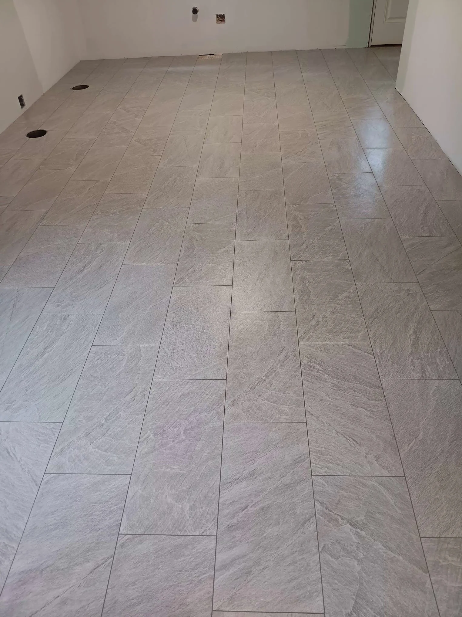 Empty room with unfinished walls, tile flooring, and three visible floor drains.