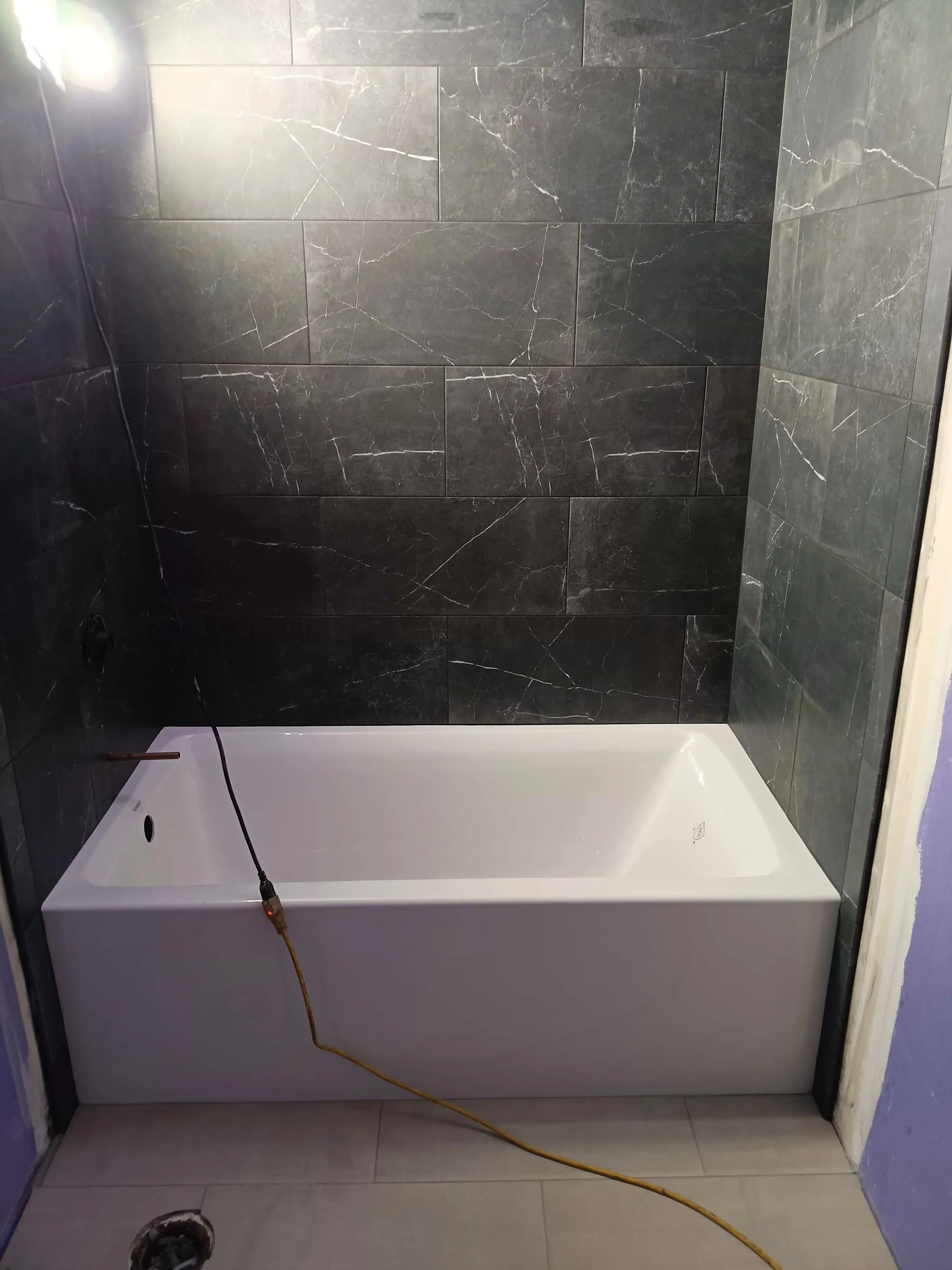 Bathroom shower area with dark tiled walls, white bathtub