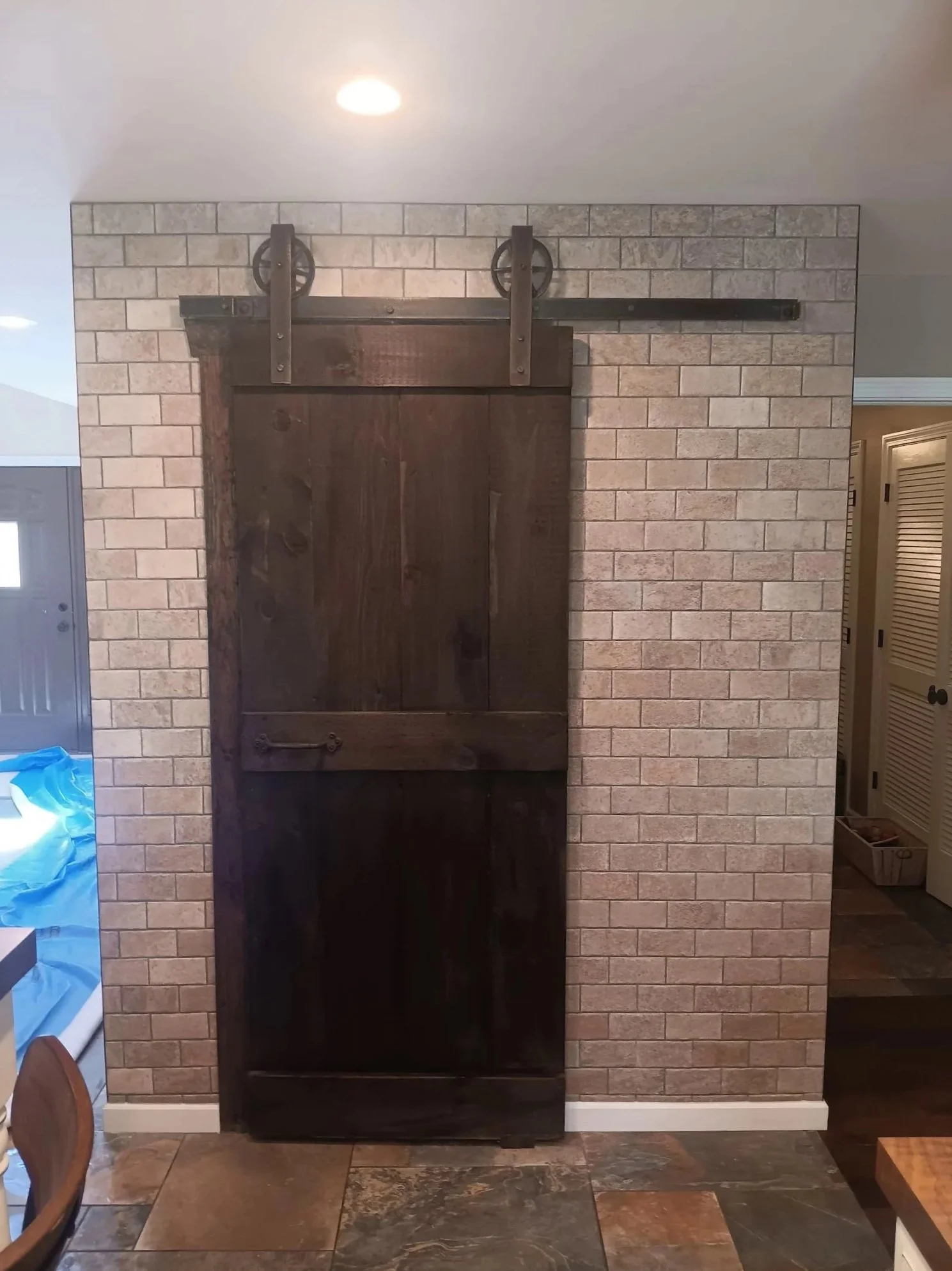 A dark wooden sliding barn door on a brick wall with a black metal track and wheels.