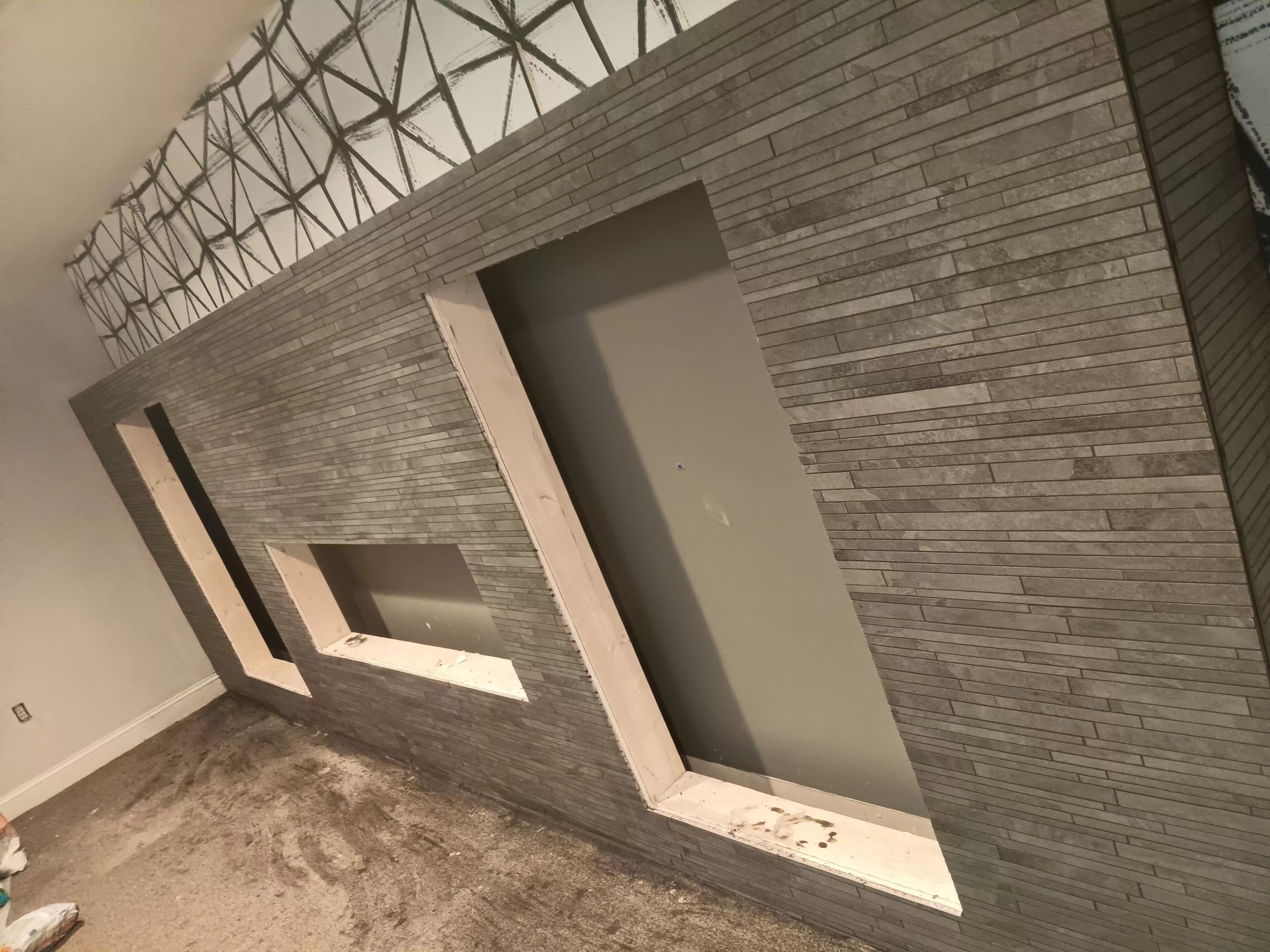 A room under construction with gray brick wall paneling, an arched opening, and a textured concrete floor.