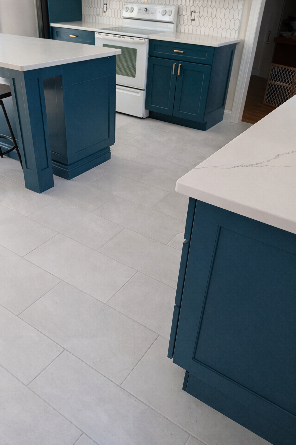 Modern kitchen with white countertops, blue cabinets, and white tile backsplash. White stove and light gray tile floor.