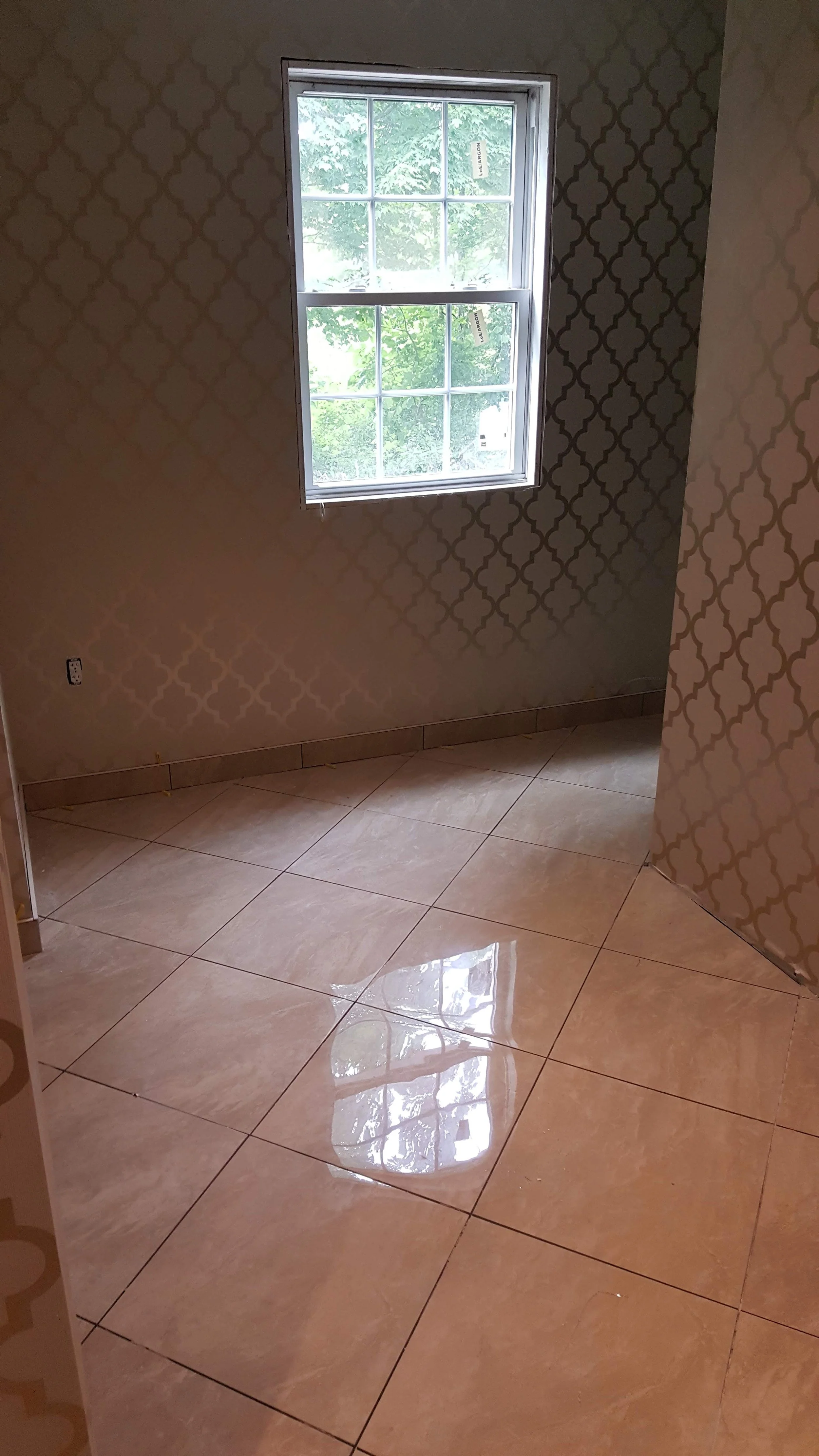 Empty room with a window, patterned wallpaper, and tiled floor.