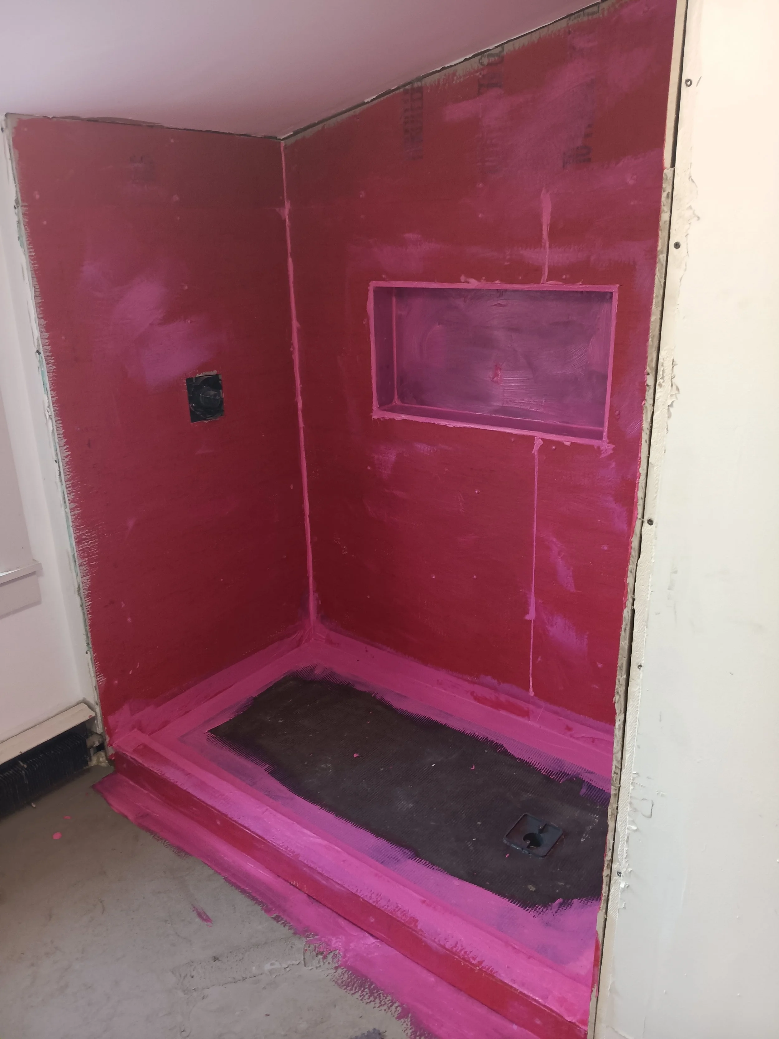 A room with pink painted walls and a black painted floor section, showing unfinished drywall borders and an electrical outlet box.