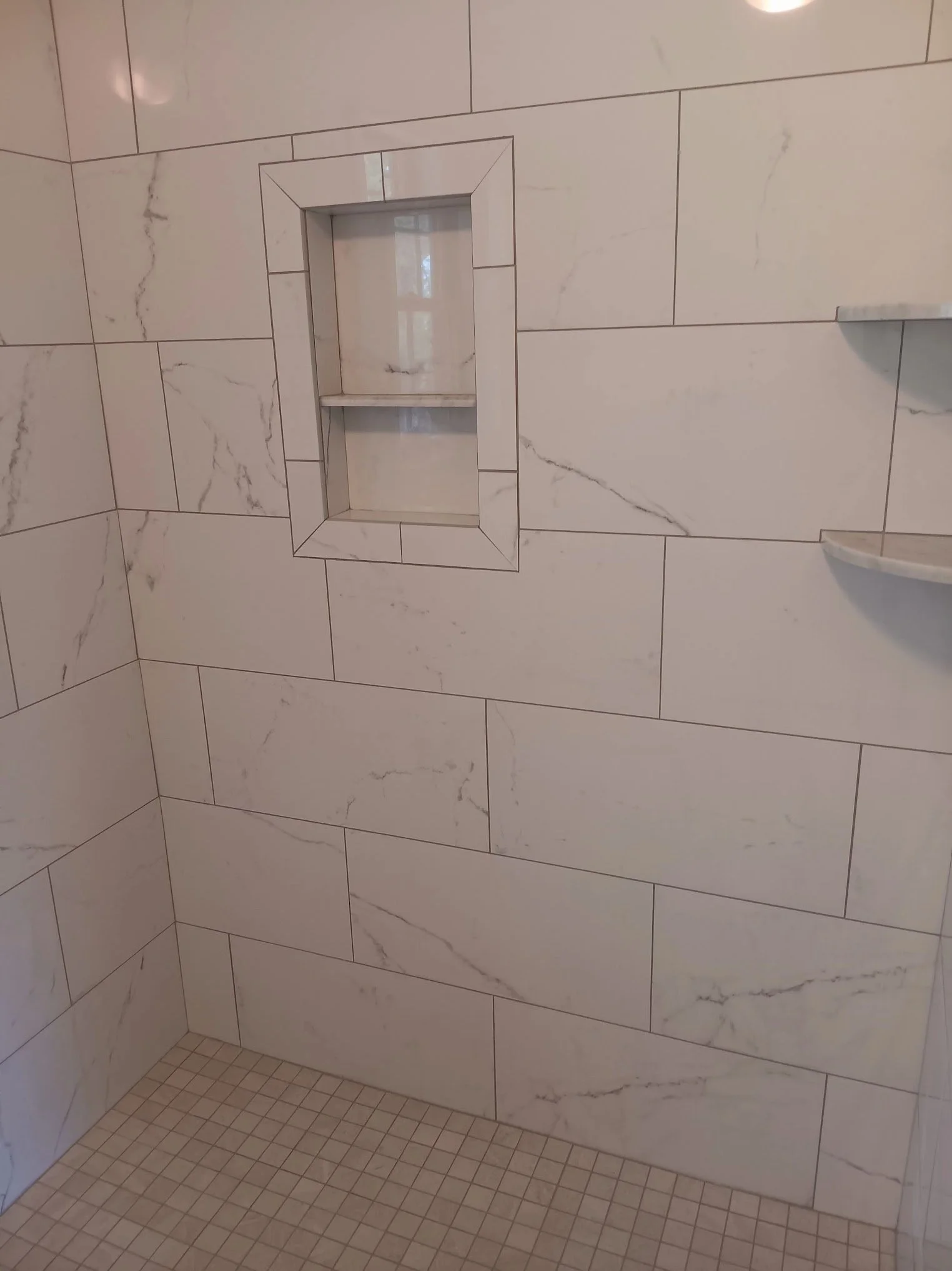 Shower wall with marble tiles, a built-in soap or shampoo shelf, and a small tiled shower floor.