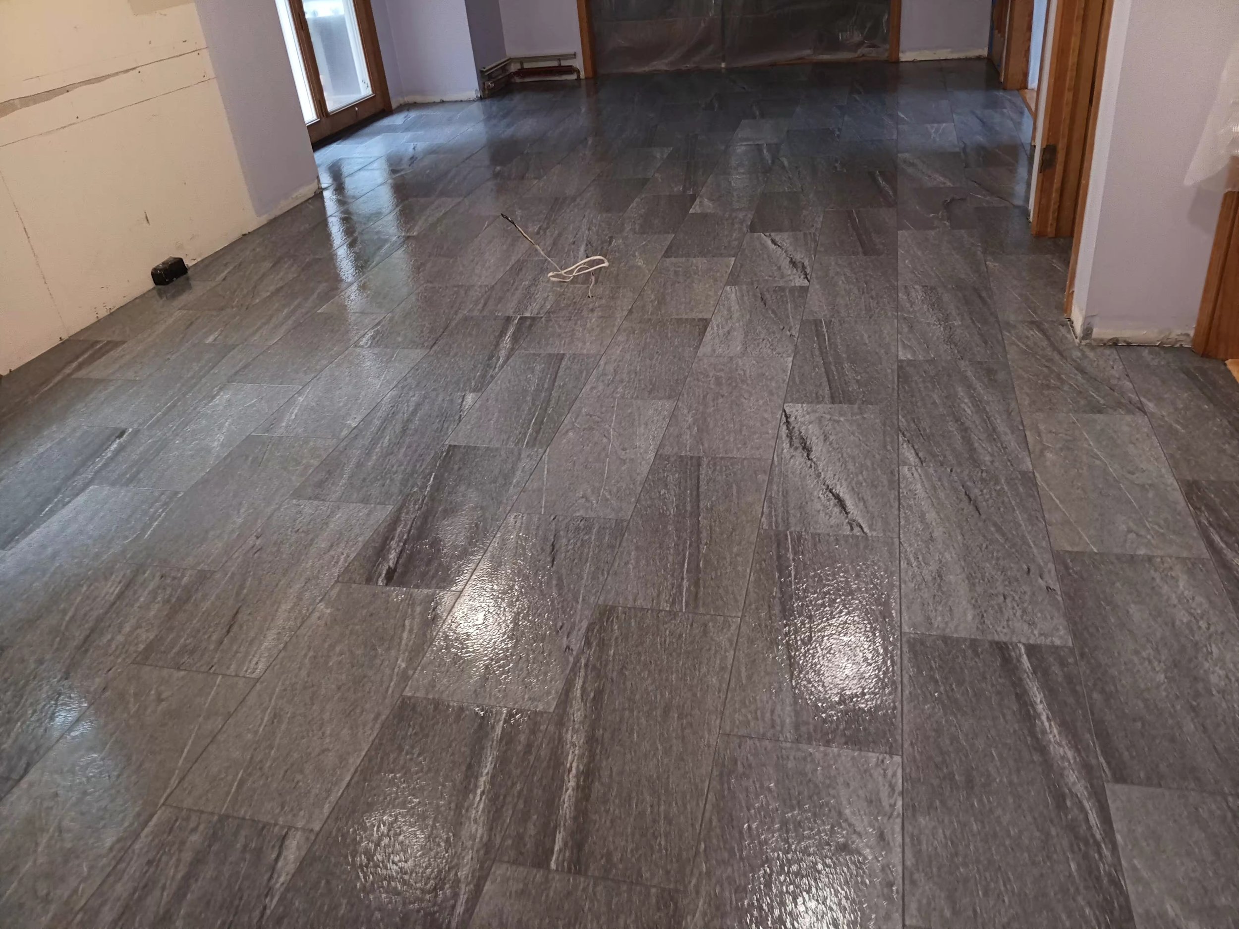 The image shows a room with newly installed dark gray ceramic tiles on the floor