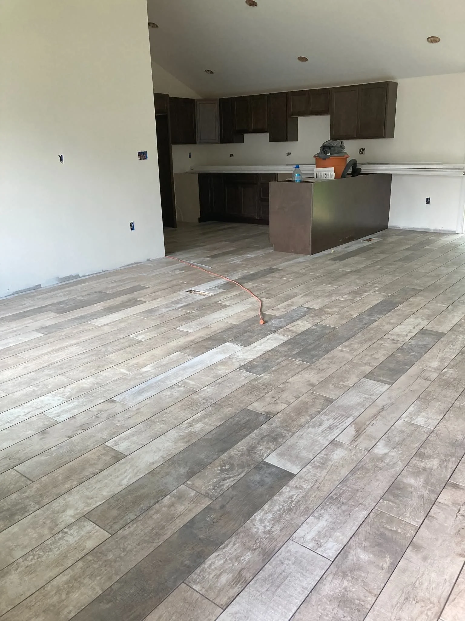 Interior of a house kitchen under renovation, with unfinished hardwood flooring and dark wooden cabinets.