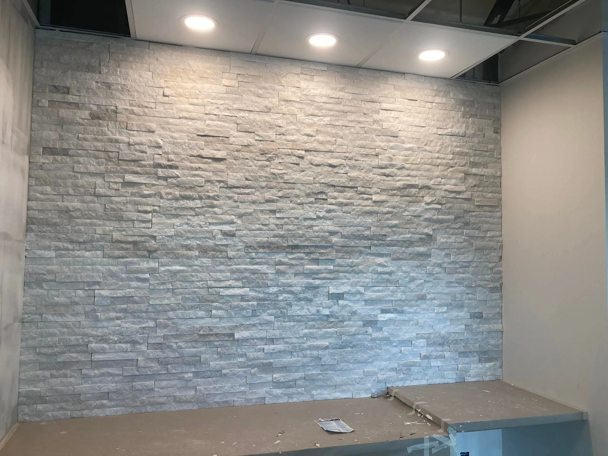 A gray stone accent wall with recessed ceiling lights in an indoor space under construction or renovation.