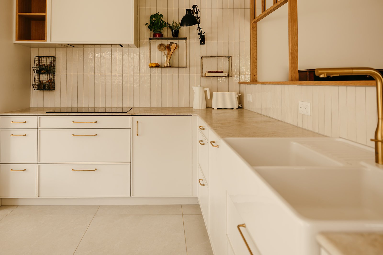 Cuisine en bois sur mesure aux façades blanches avec plan de travail en pierre naturelle et poignées en laiton réalisée par Atelier Set