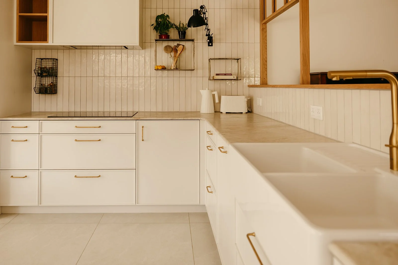 Cuisine en bois sur mesure aux façades blanches avec plan de travail en pierre naturelle et poignées en laiton réalisée par Atelier Set