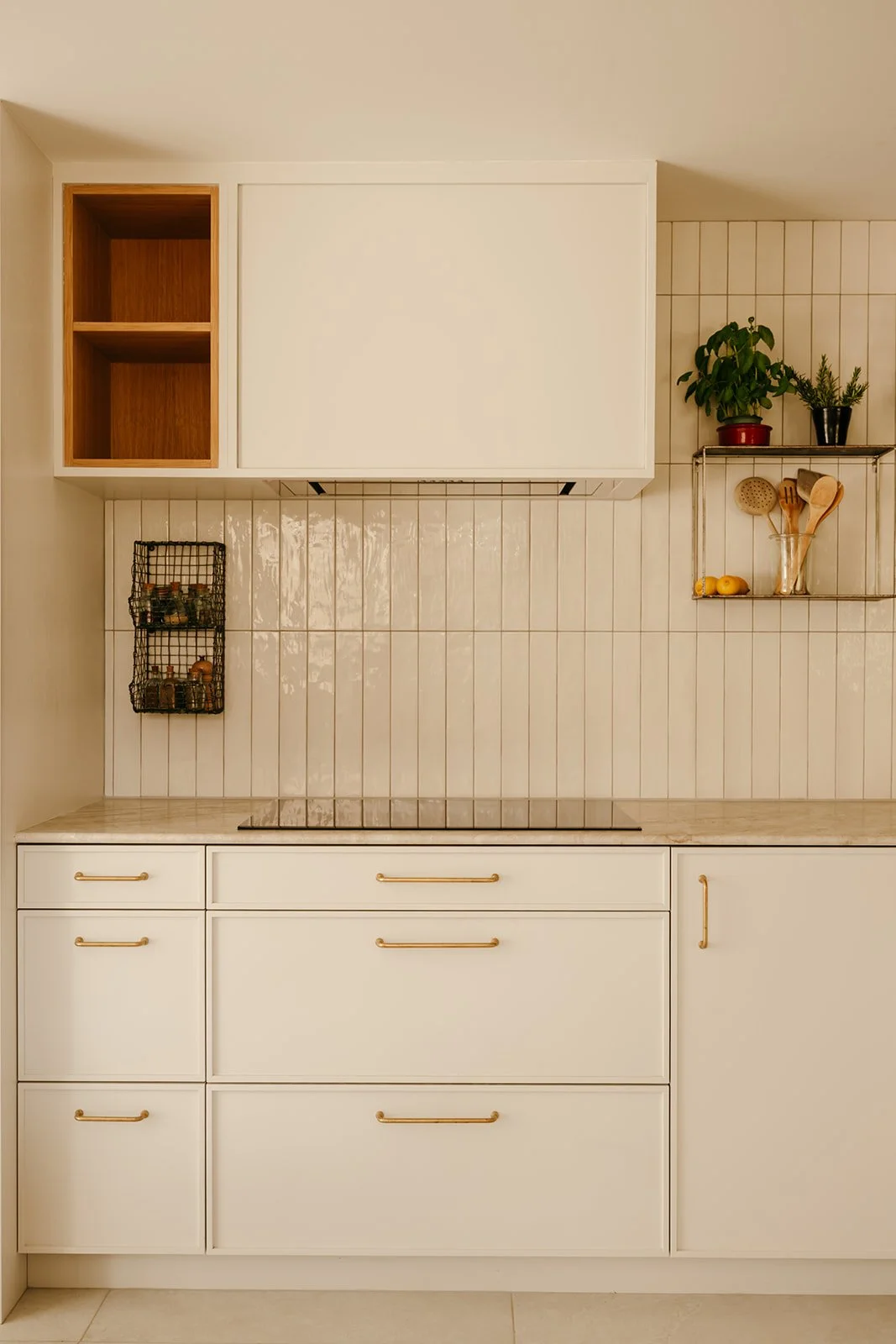 Cuisine blanche avec plan de travail en pierre naturelle, plaque de cuisson, hotte intégrée et niches de rangement latérales.