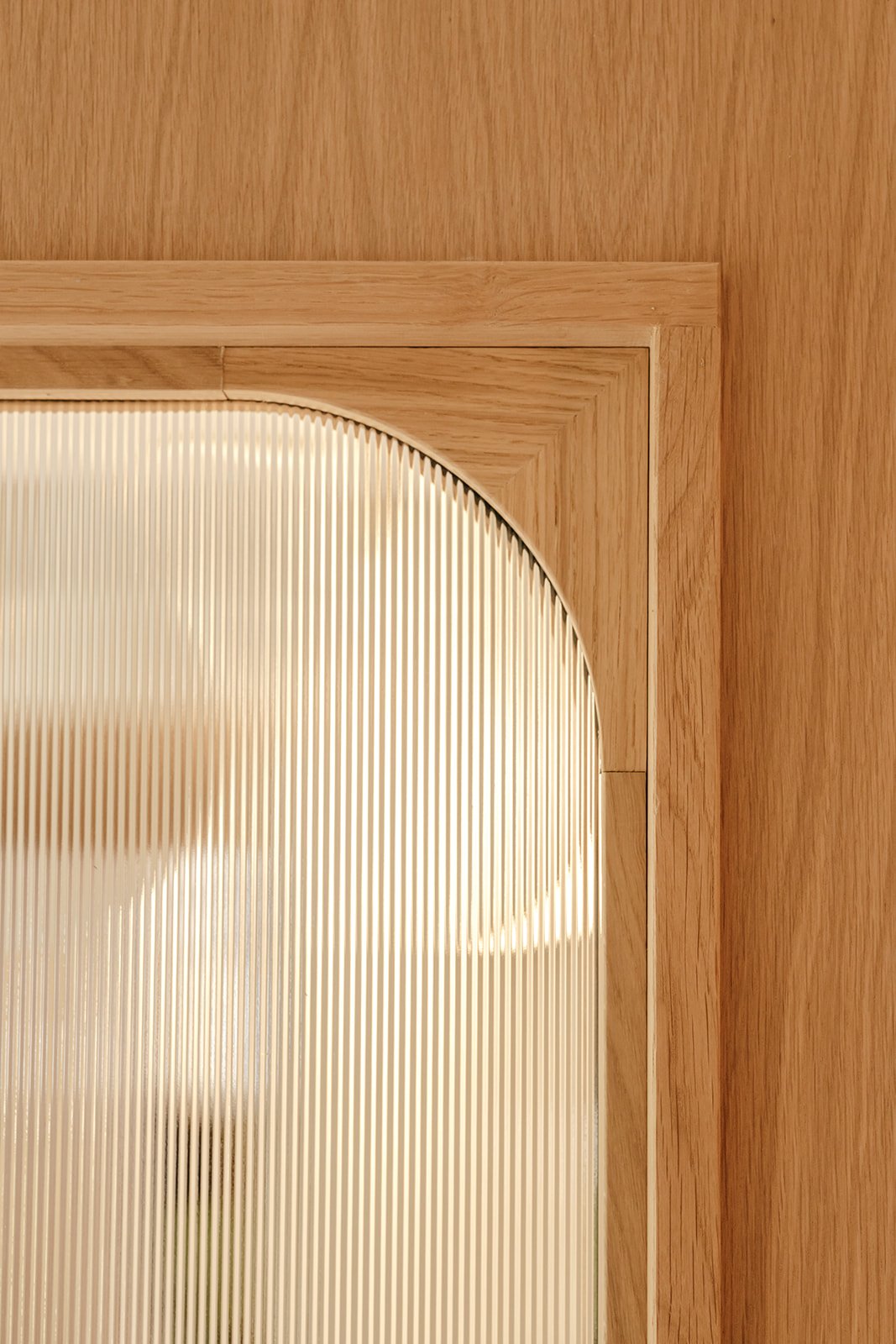 Détail d'une fenêtre intérieure en bois avec angles arrondis et verre strié