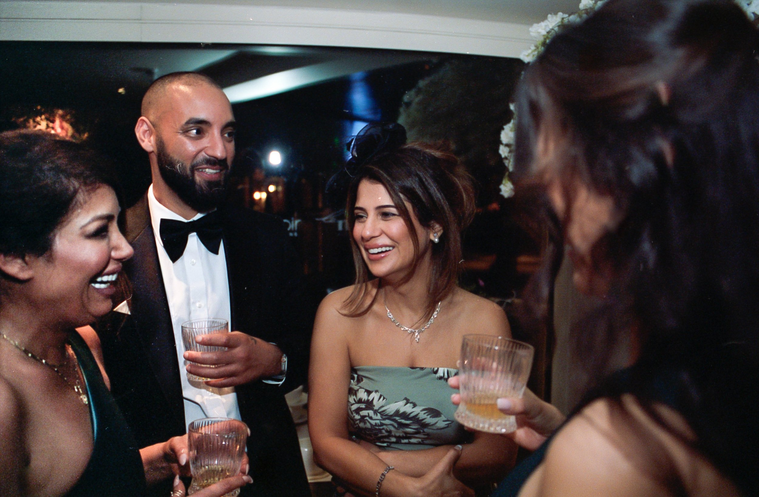 A group of five adults dressed formally at a social event, holding drinks and engaging in conversation.