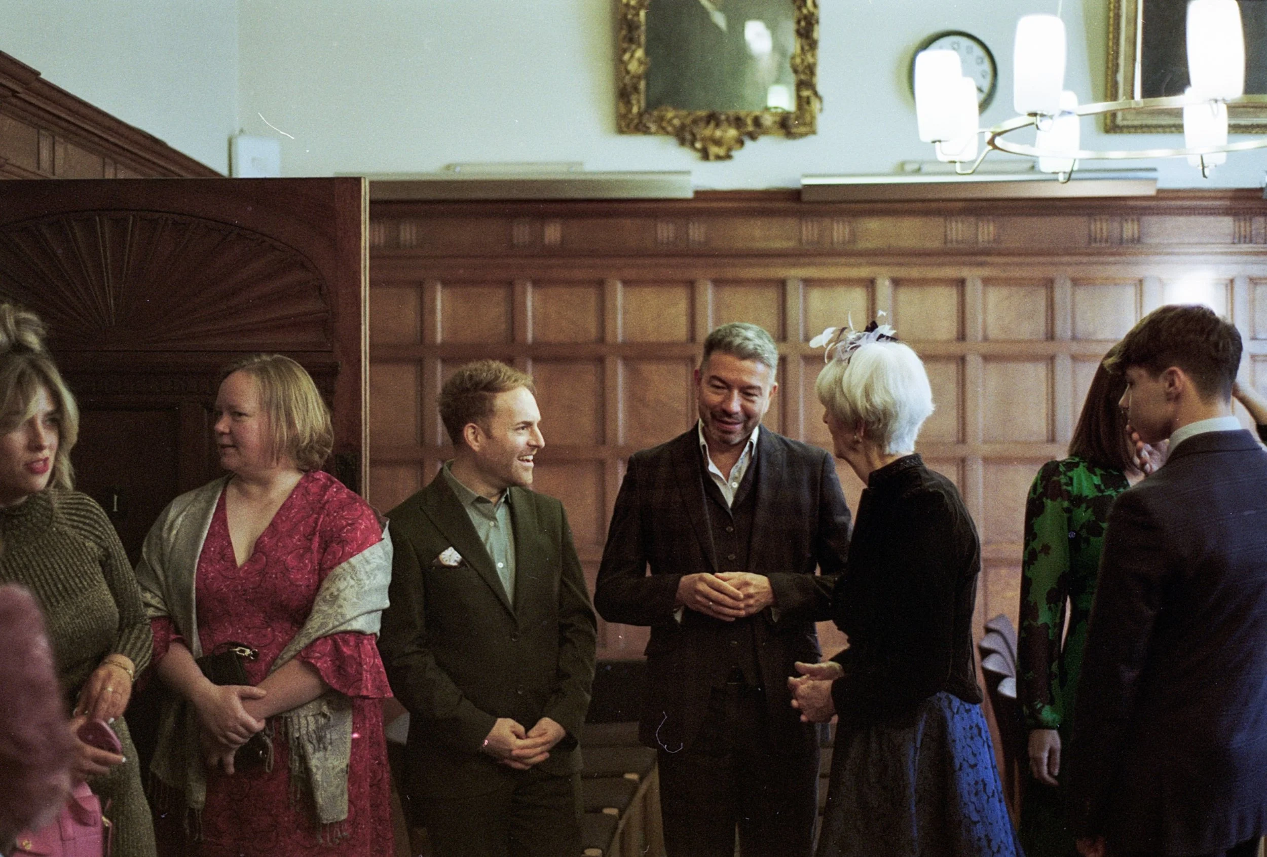 People gathered in a formal room, engaging in conversation, dressed in elegant clothing.
