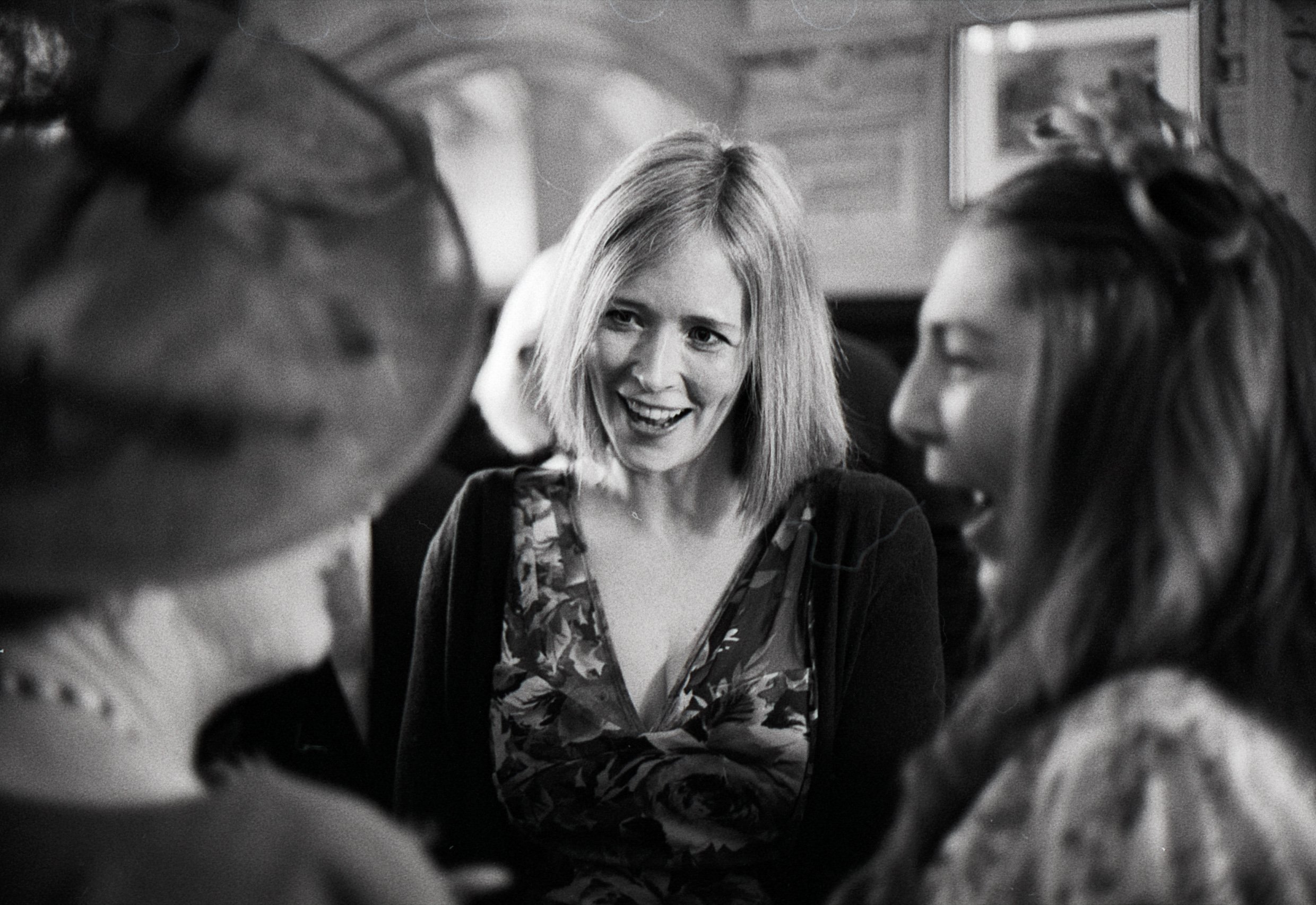 Three women engaged in conversation in a cozy indoor setting with wooden walls, smiling and appearing to enjoy each other's company.