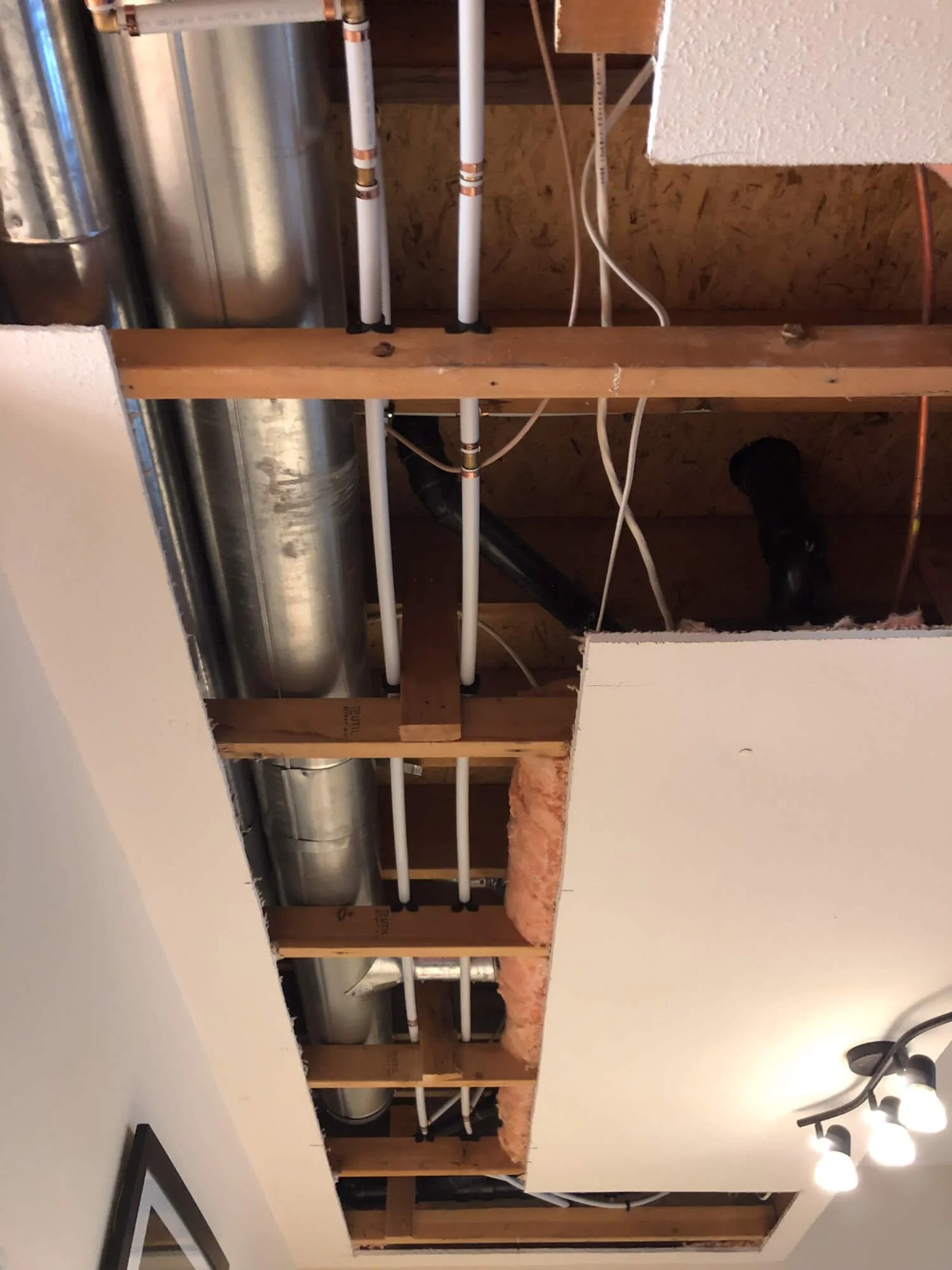 Exposed residential plumbing and HVAC ducting during a whole-home repiping project in the Okanagan.