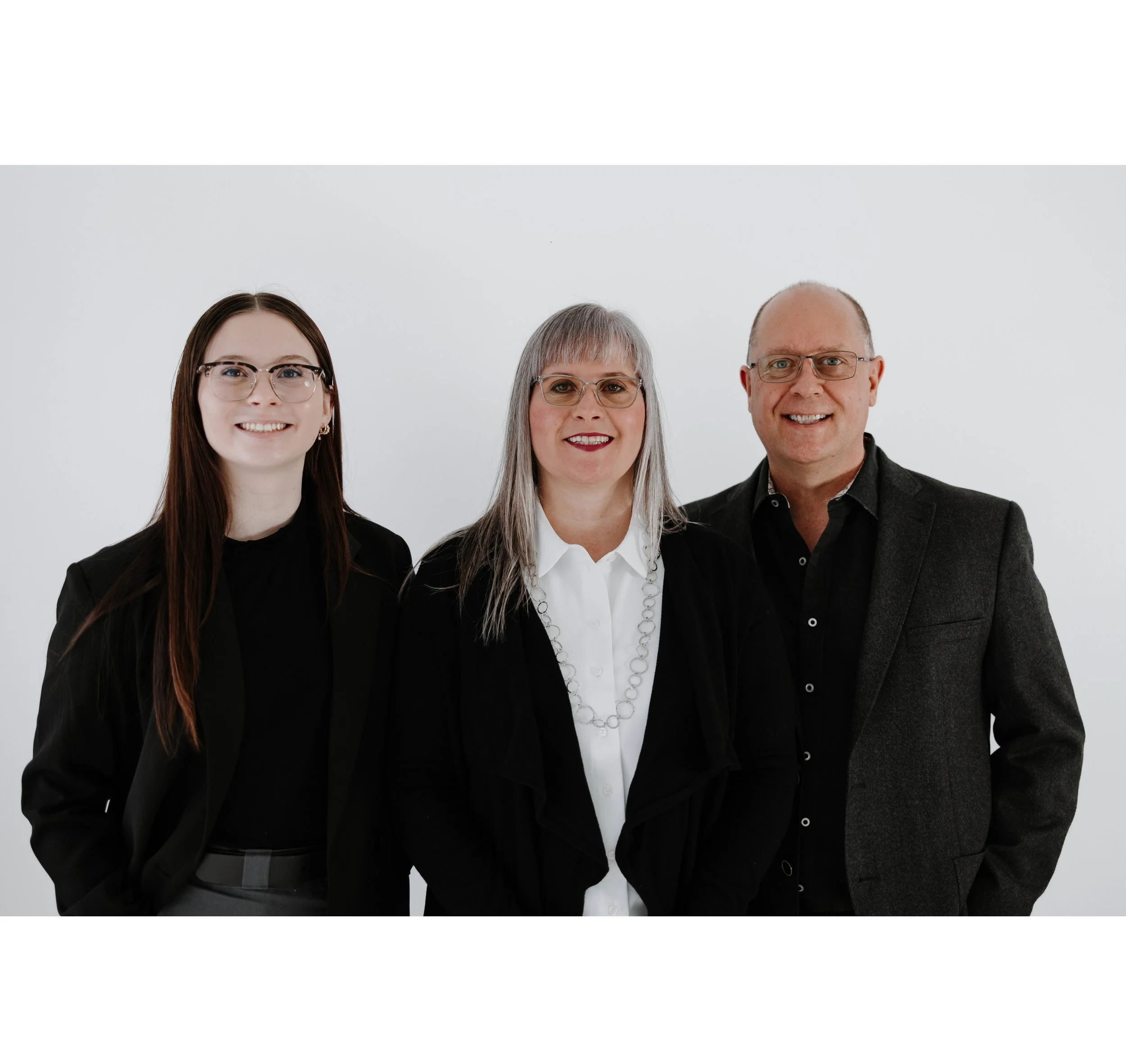 Three professionally dressed REALTOR adults, two women and one man, standing against a plain white background, smiling at the camera.