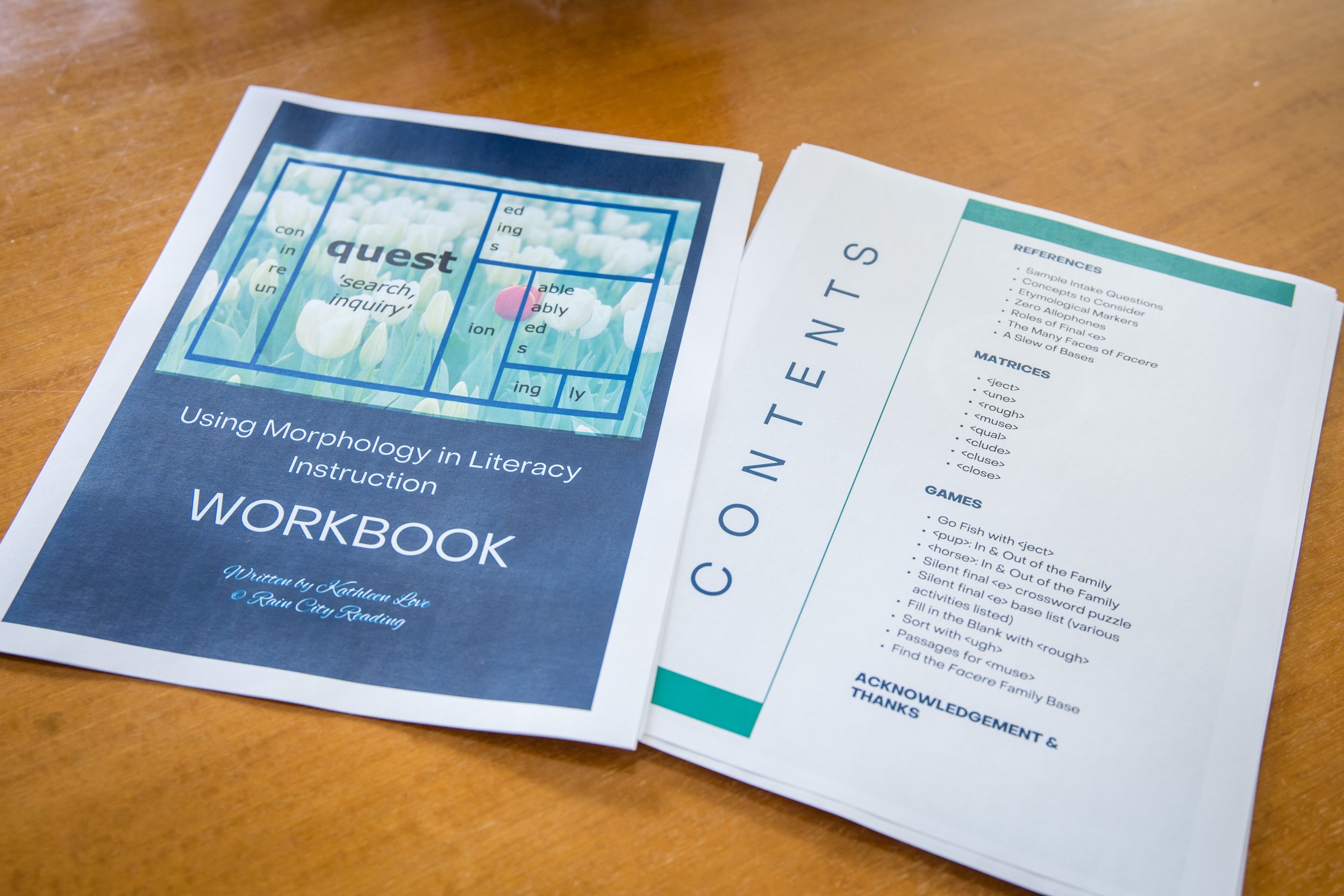Close-up of educational worksheets on a wooden table, one titled 'Using Morphology in Literary Instruction Workbook' featuring a crossword puzzle with words like quest, search, inquiry, able, capable, and study, and another with references and game activities.