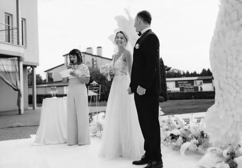 Black and white photo of a wedding ceremony outdoors with bride, groom, and officiant.