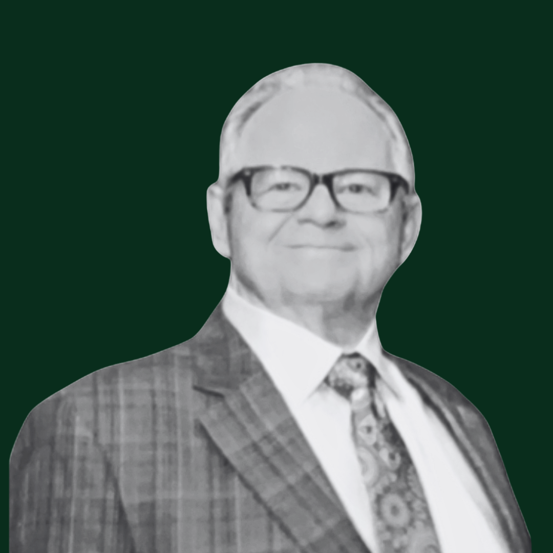 Black and white photo of The Tunney Group's CEO, Edward Tunney, wearing glasses, a plaid suit, white shirt, and patterned tie, standing against a dark background.