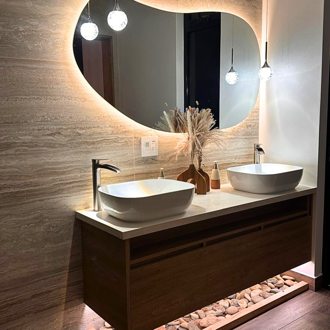 Modern bathroom vanity with two vessel sinks, oval mirrors with backlighting, decorative vases, and hanging pendant lights.