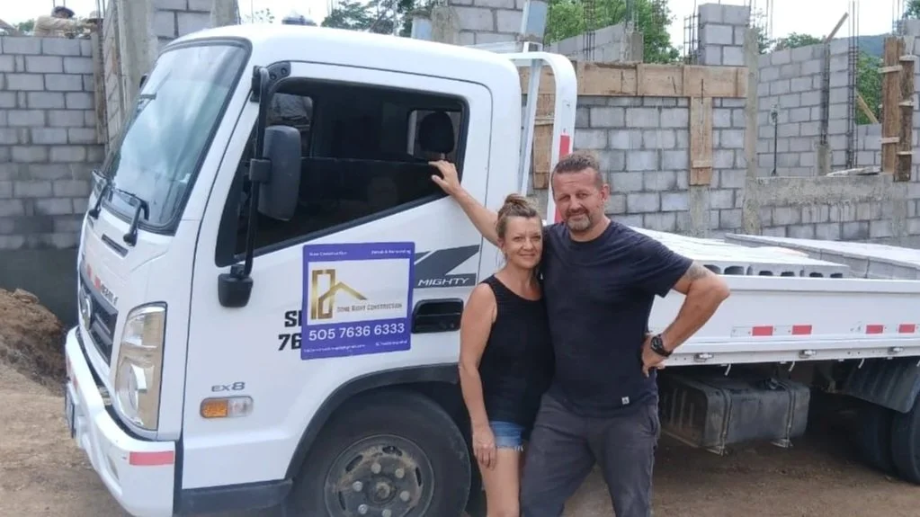 Our founders, Robert and Agnes, standing together in front of a white construction truck at a building site, with unfinished brick walls in the background.
