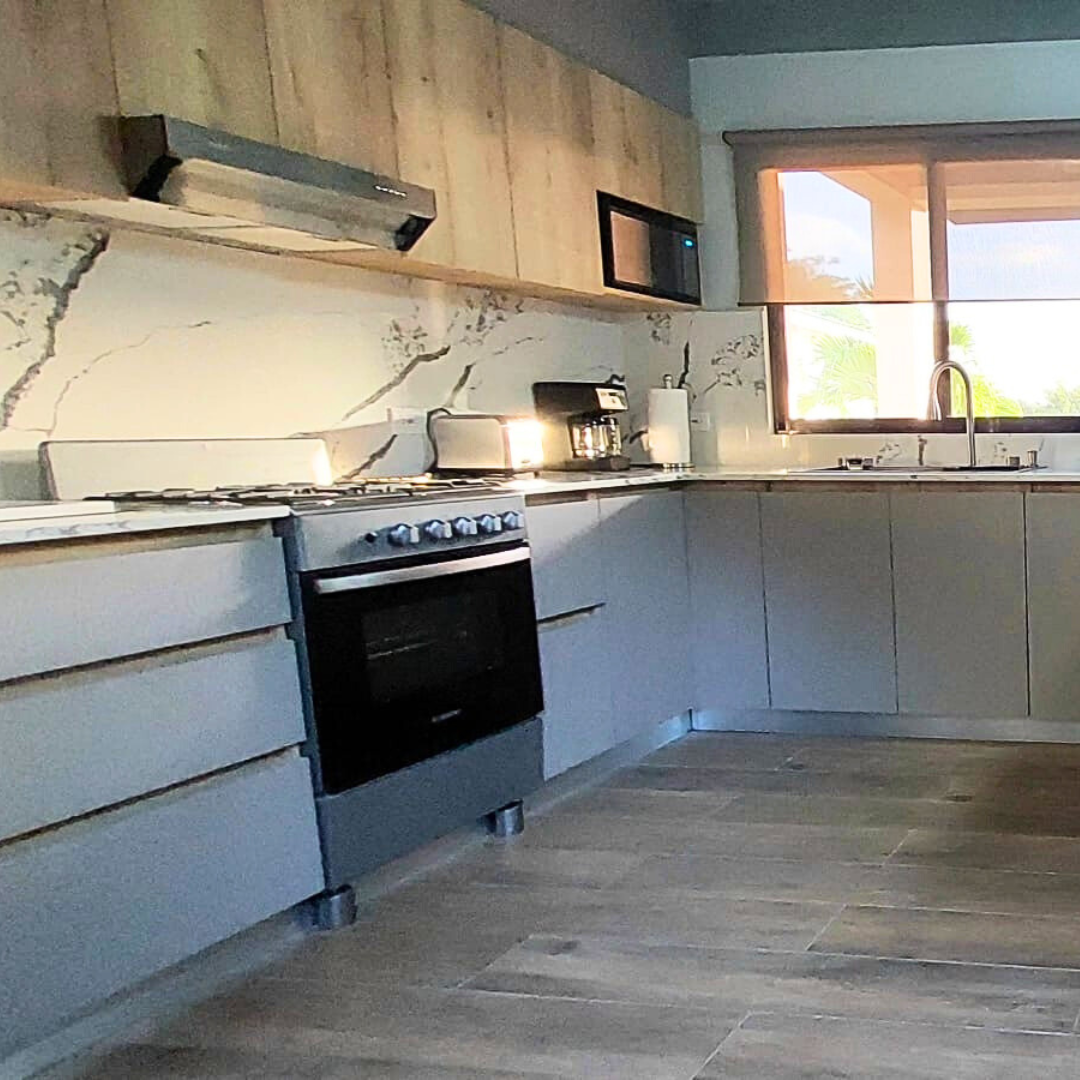 Modern kitchen with gray cabinets, marble backsplash, wooden upper wall, window, and stainless steel appliances.
