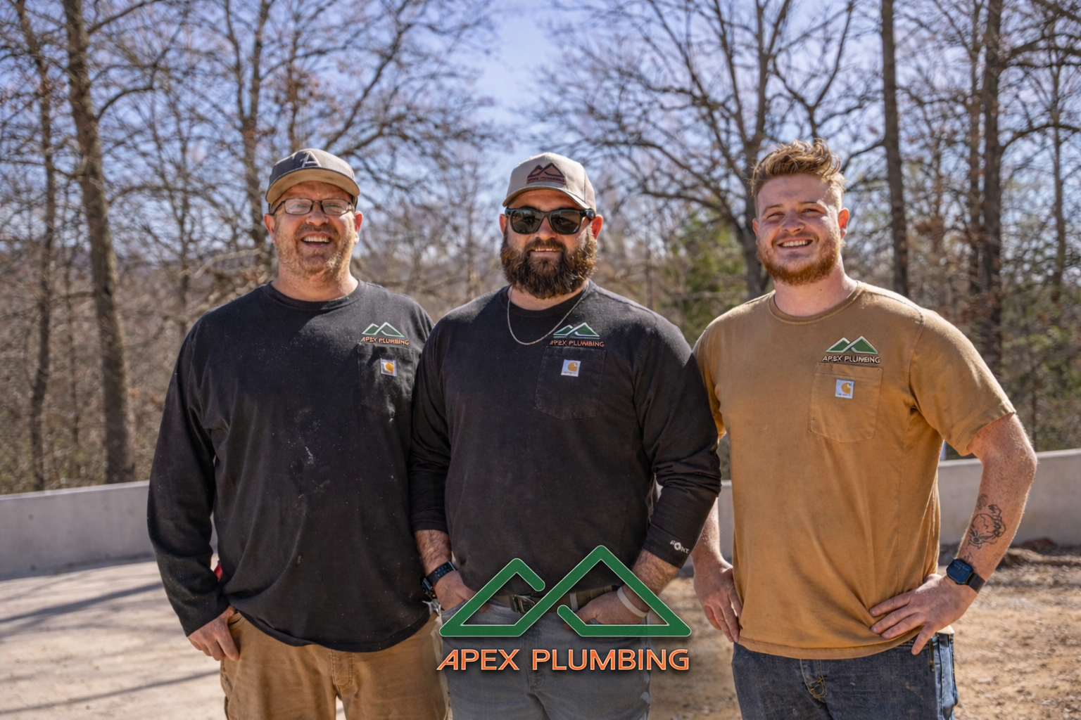 Three men standing outdoors with trees in the background, wearing shirts with the Apex Plumbing logo, smiling at the camera.