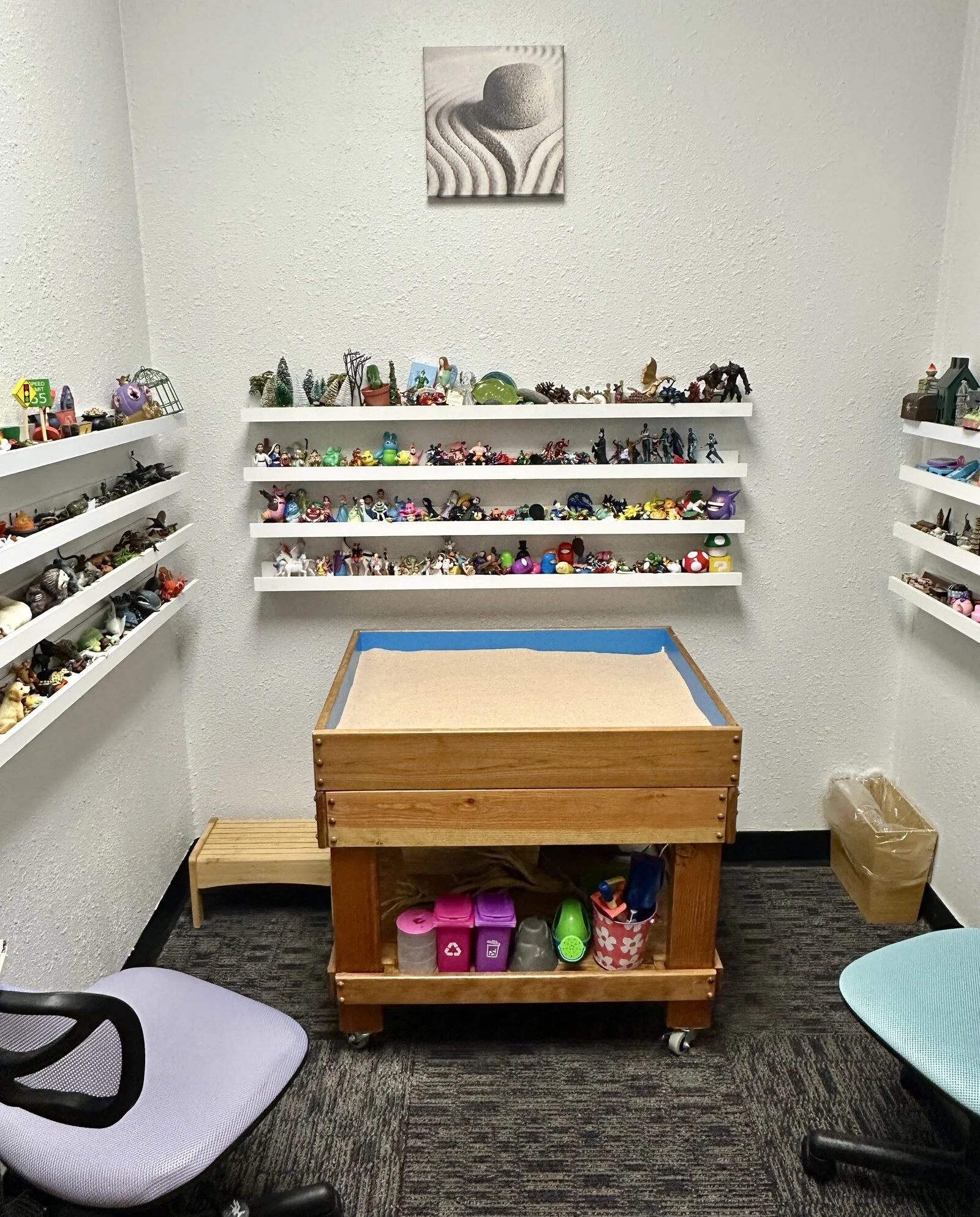 A tray of sand with shelves full of miniatures behind it.