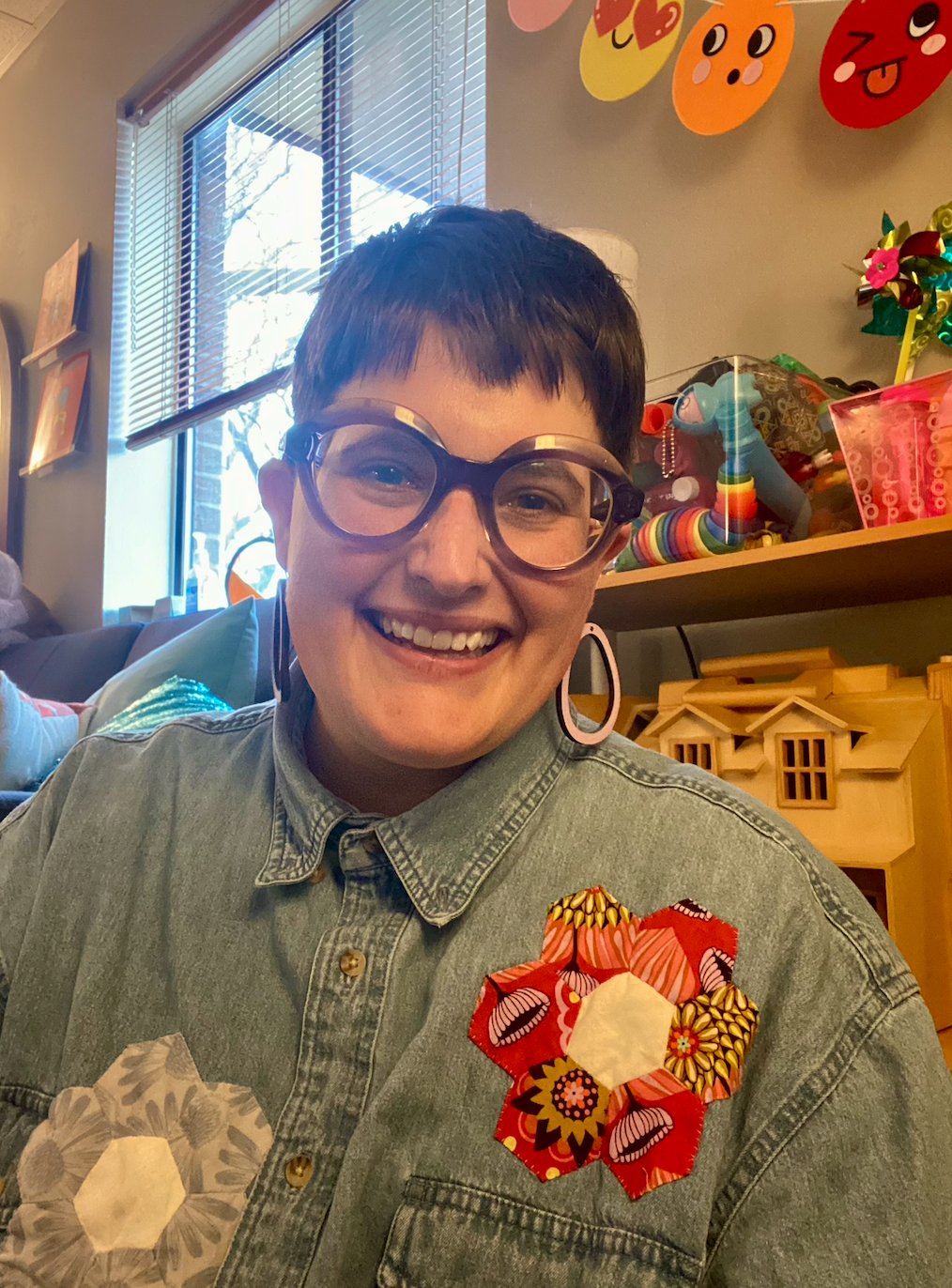 Photo of Ren, a White person with short hair and glasses smiling in a playroom