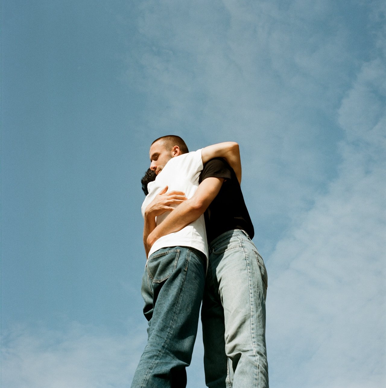 Two people hugging each other against a blue sky with some clouds.