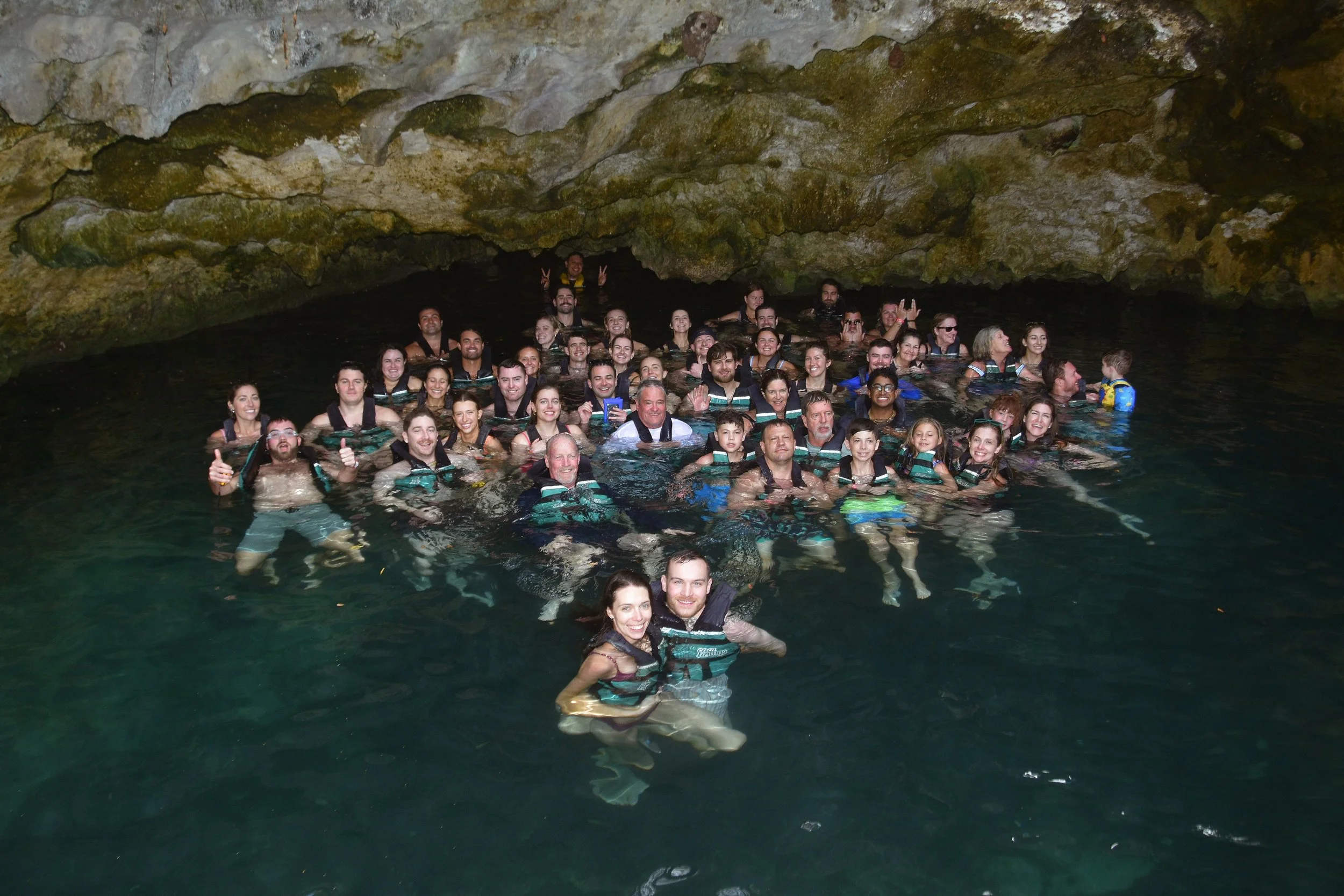 A large group of people swimming and posing for a photo inside a cenote cave in Tulum, Mexico while on a company brand trip.