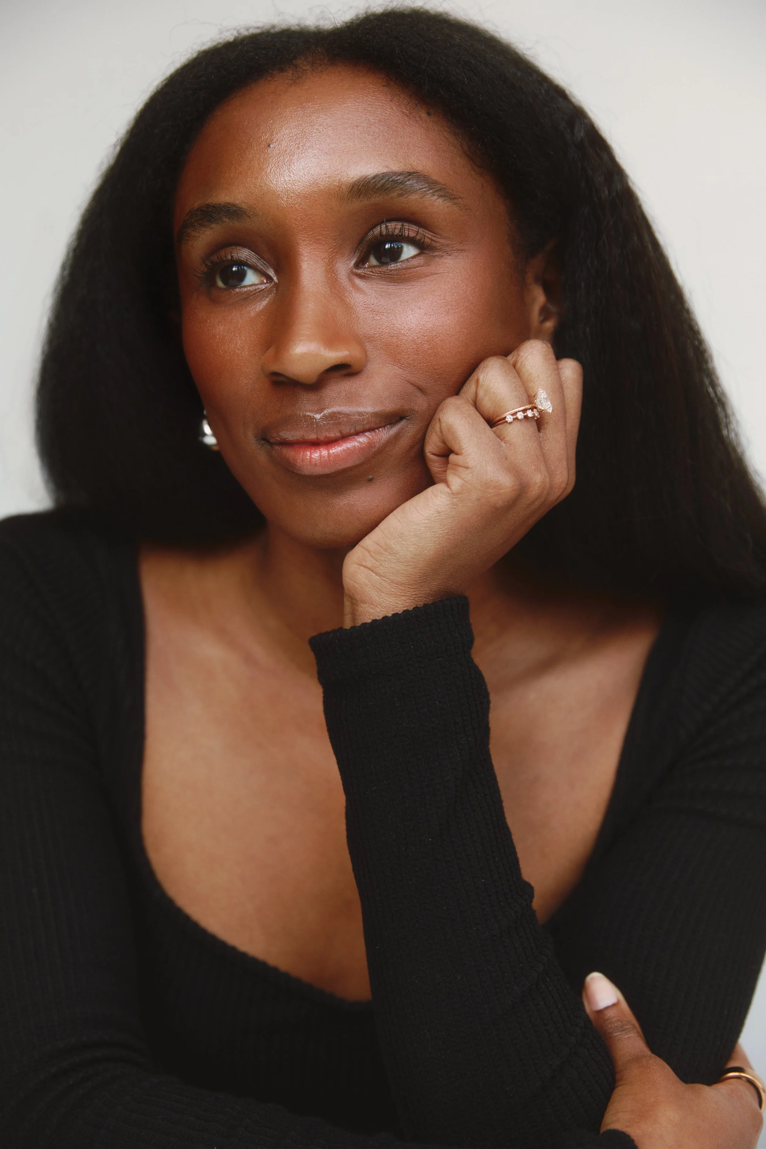 Close-up of a woman with dark hair, wearing a black top, resting her chin on her hand, and looking thoughtfully to the side.