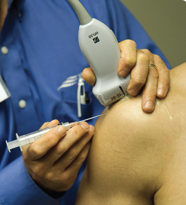 Medical professional administering an ultrasound or injection on a patient's shoulder.