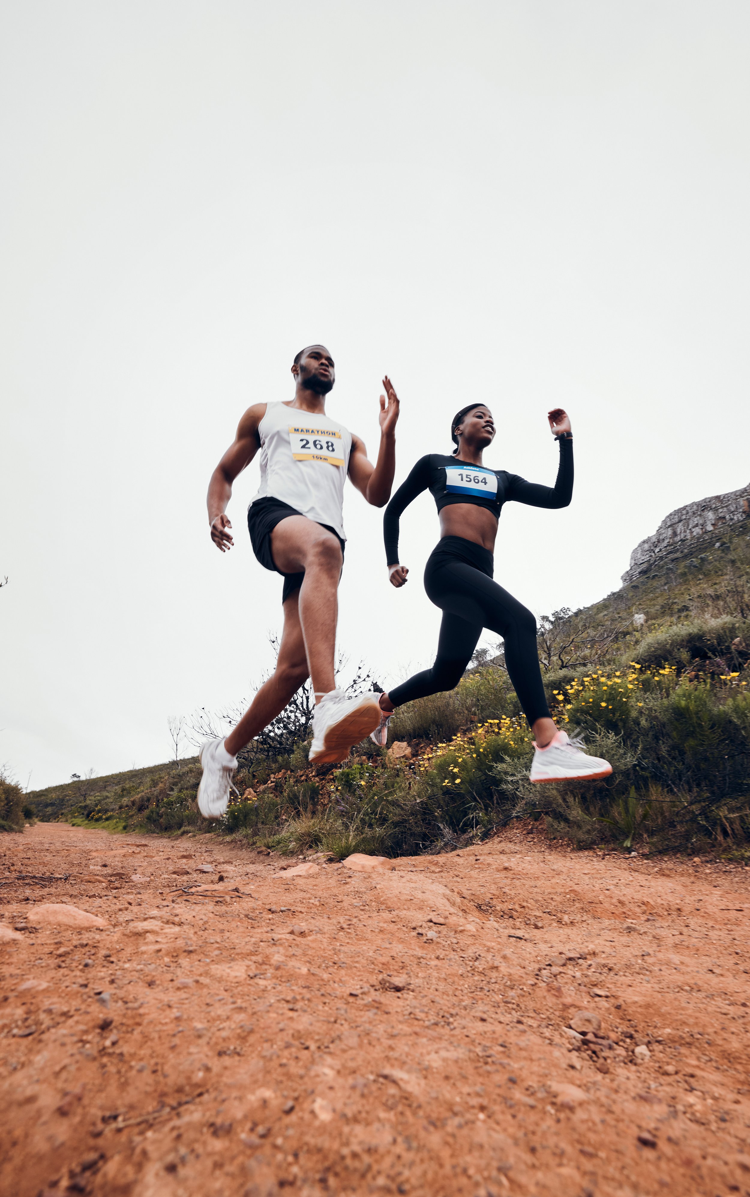 Two runners participating in a trail race on a dirt path with natural landscape and overcast sky.