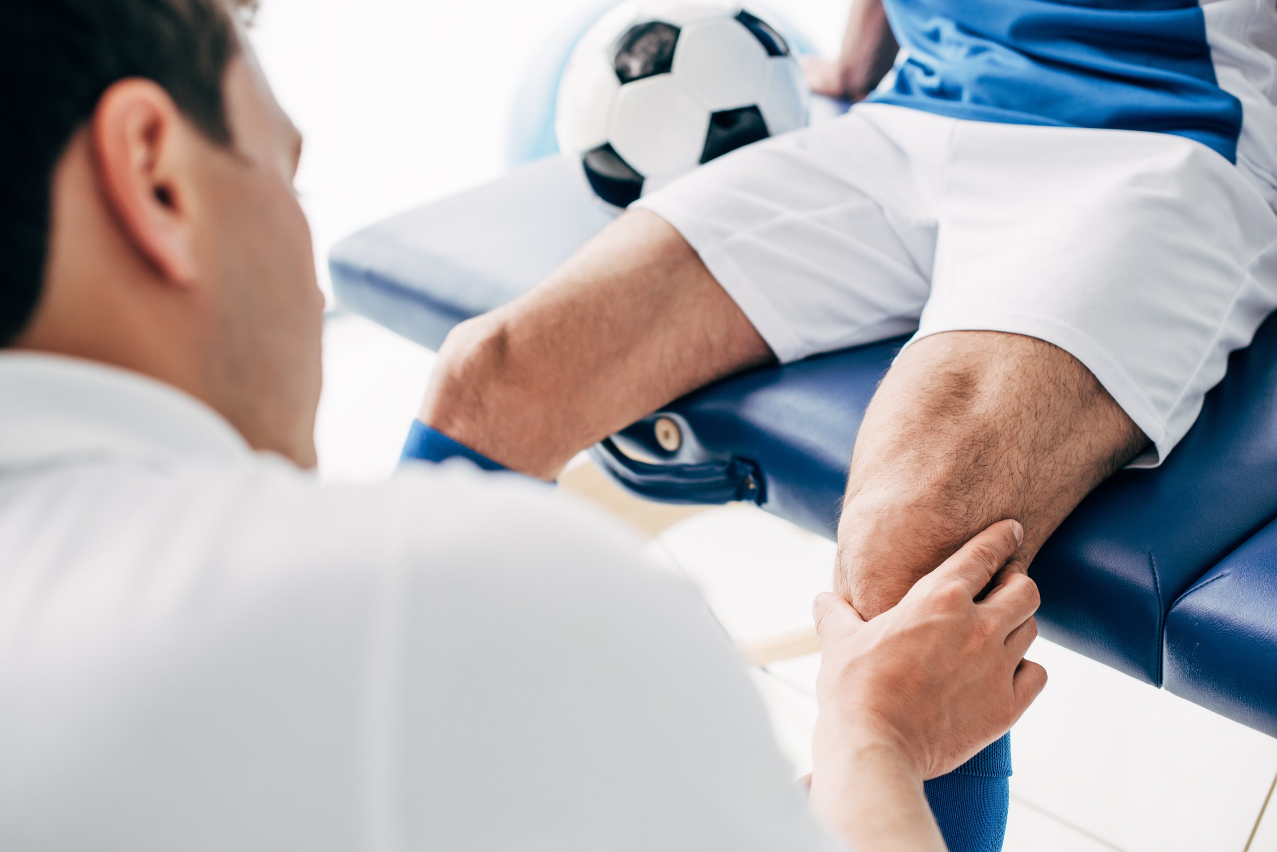 Doctor examining patient's leg with a football on a examination table