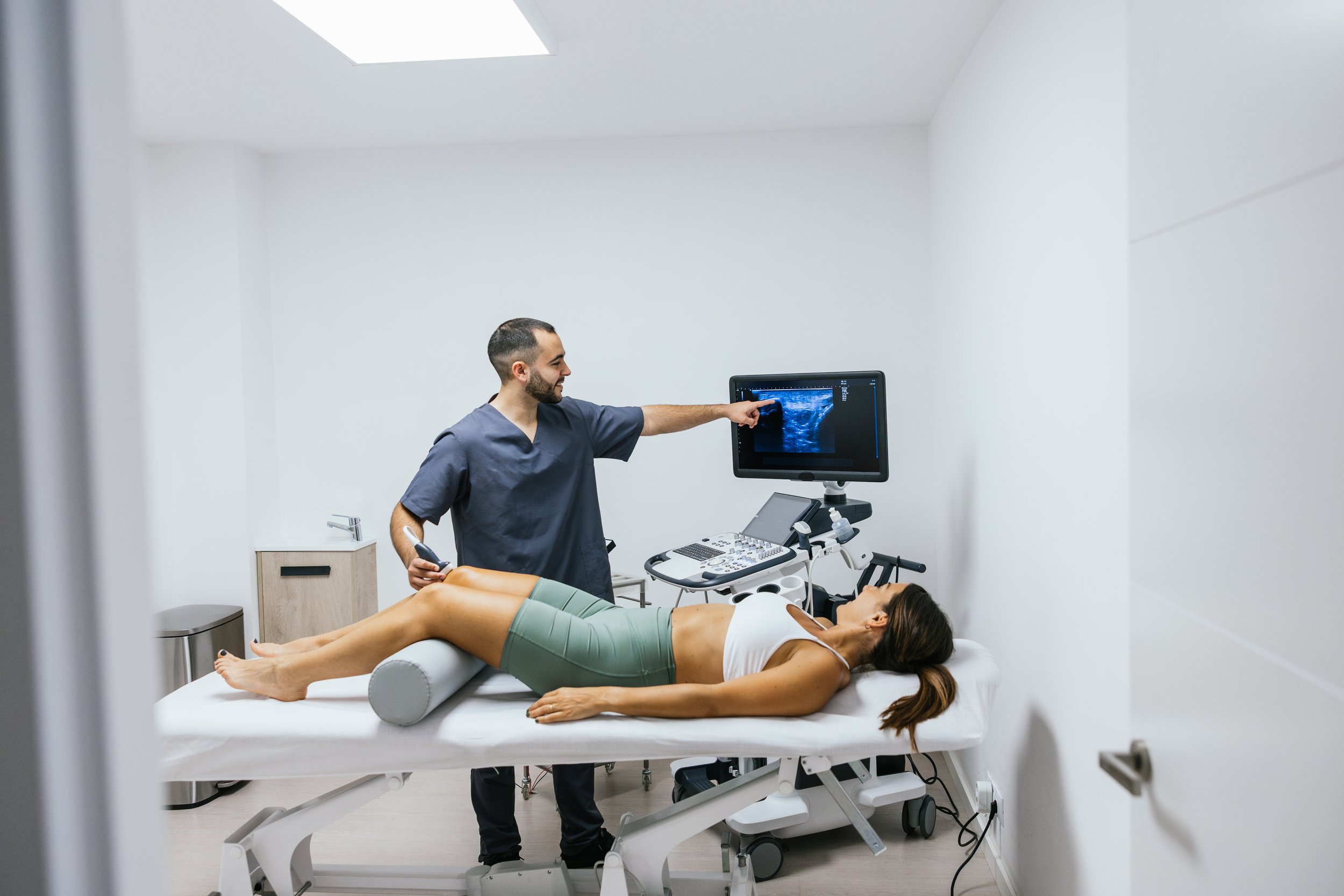 Medical professional conducting an ultrasound on a patient lying on an examination table in a clinical setting.