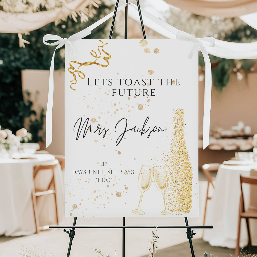 Wedding countdown sign with gold accents and champagne glasses illustration at an outdoor celebration.