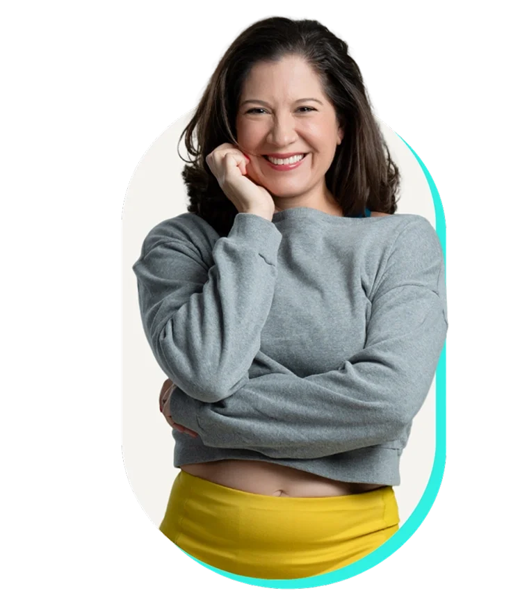 A woman smiling, wearing a gray sweatshirt and yellow pants, with her hand on her chin.