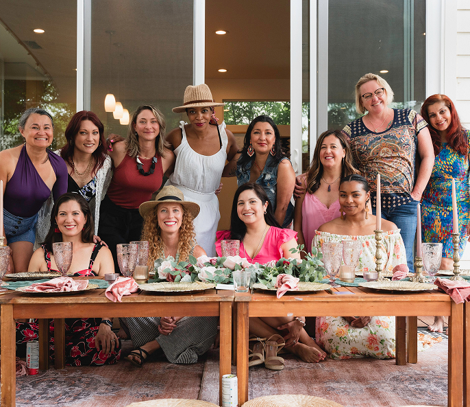 Group of women gathered around a dinner table, smiling for a photo during a celebration or gathering.