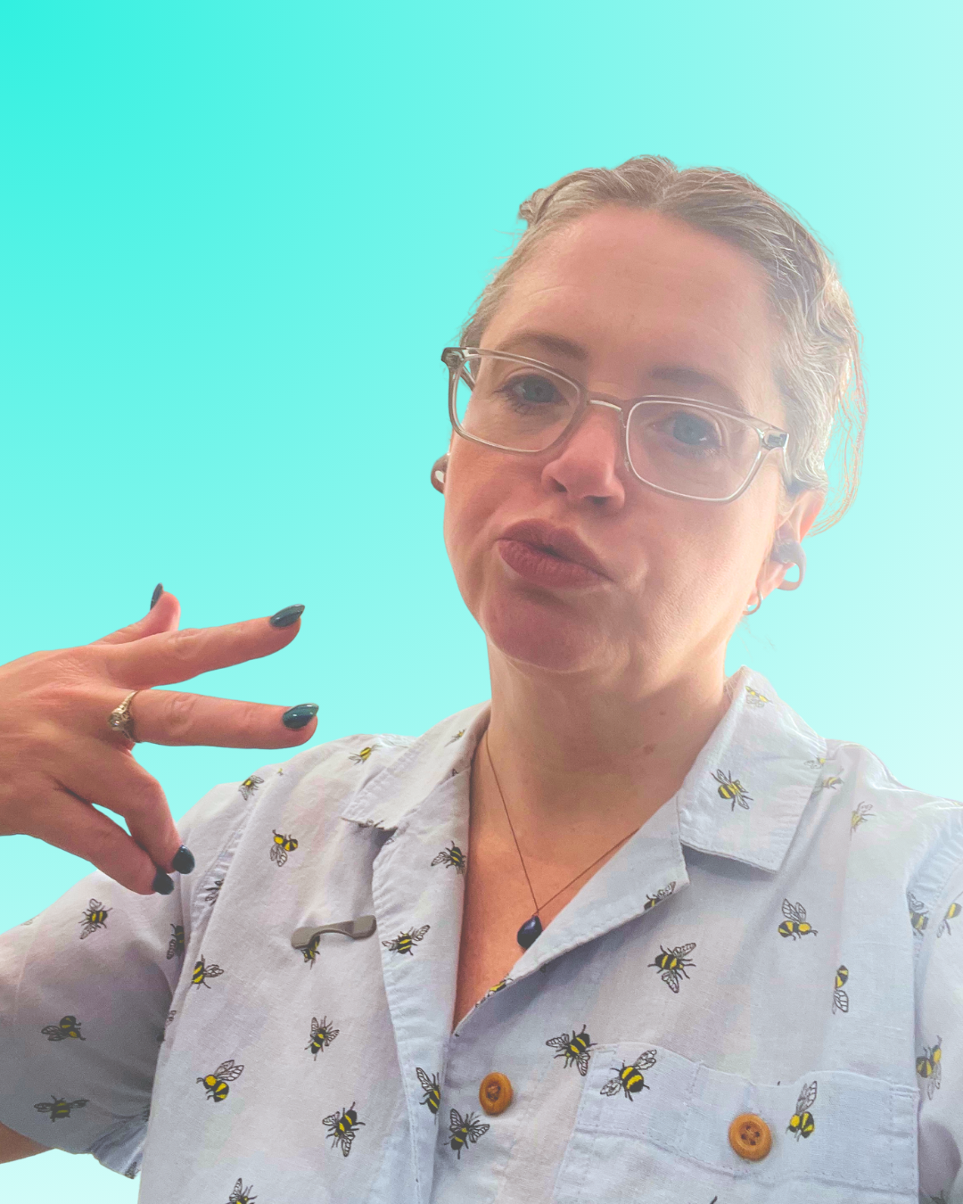 Person with short, blonde hair wearing glasses, a bee patterned shirt, posing with a peace sign against a gradient light turquoise background.