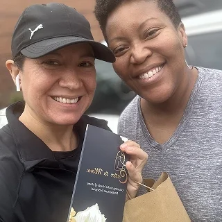 Two women smiling and taking a selfie together, with one holding a gift bag and a chocolate box.