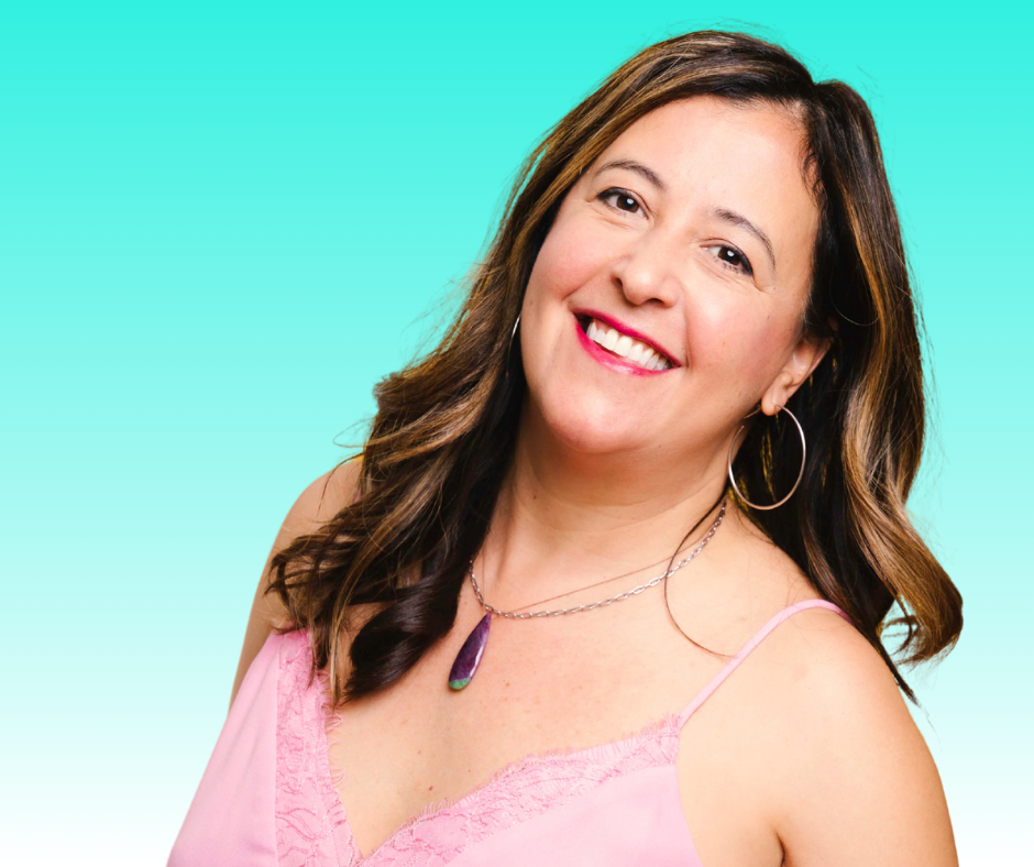 Portrait of a woman with brown hair wearing a pink top and jewelry, smiling against a turquoise background.