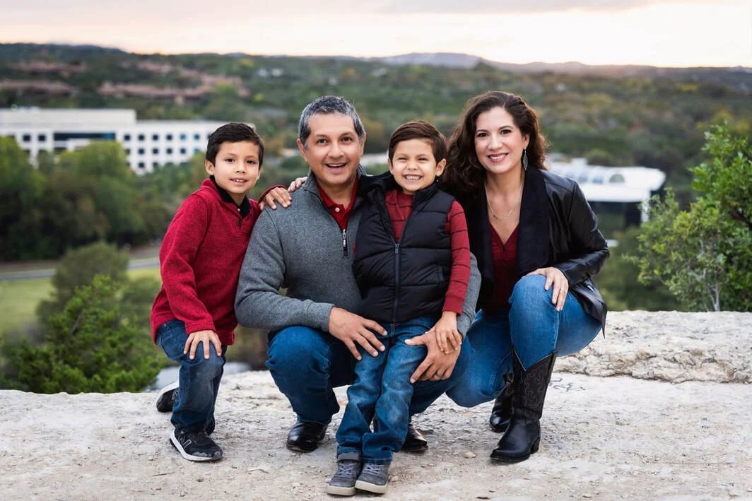 A happy family of four outdoors on a rocky surface with a cityscape and hills in the background, posing for a photo.