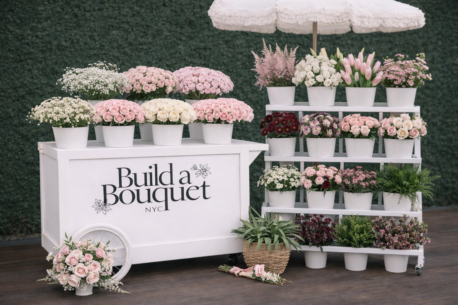 Display of various pink, white, and purple flowers in white pots at Build a Bouquet NYC floral shop with a white cart and greenery background.