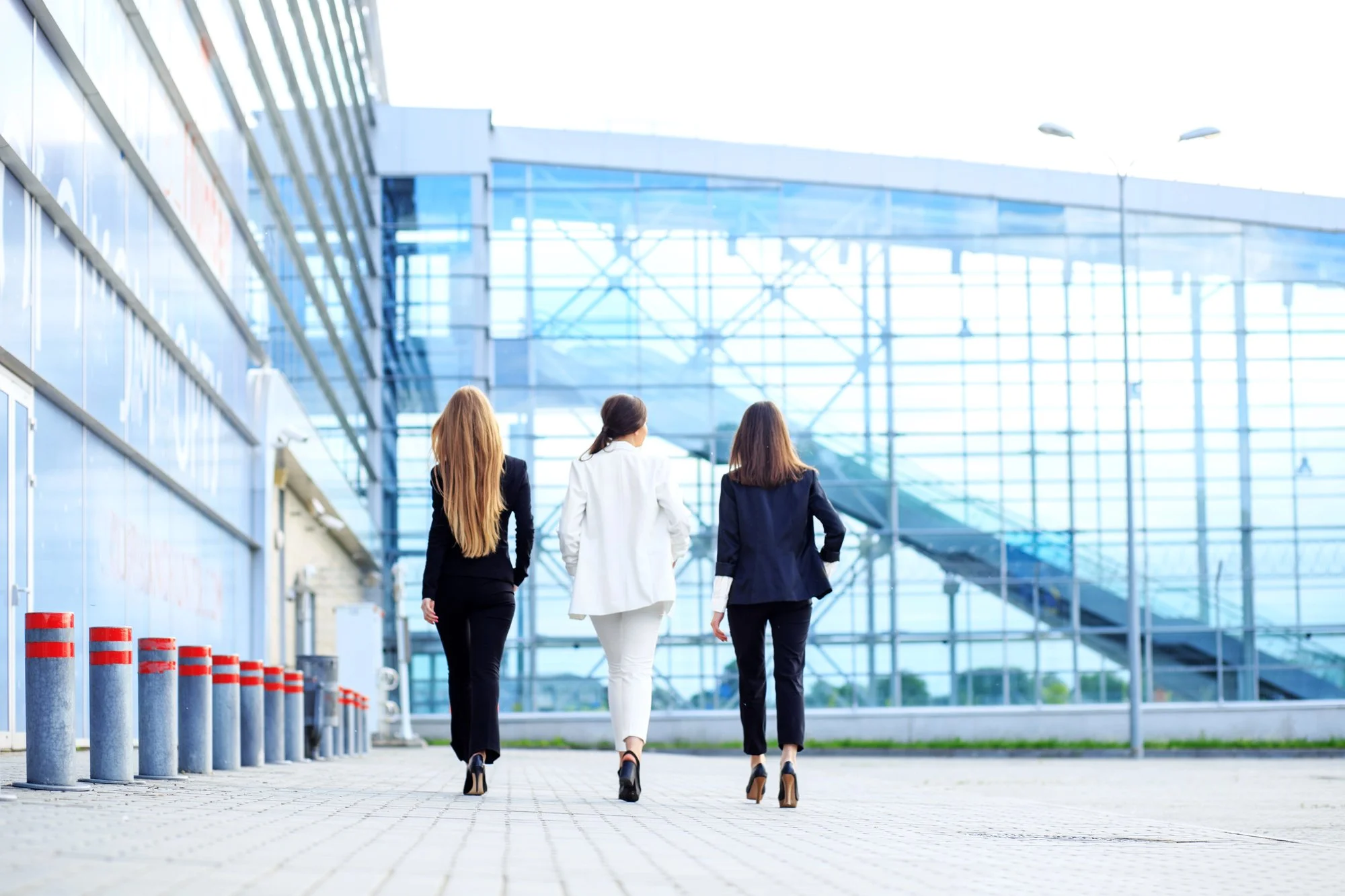 Three women in business attire walking away from the camera towards a modern glass building.