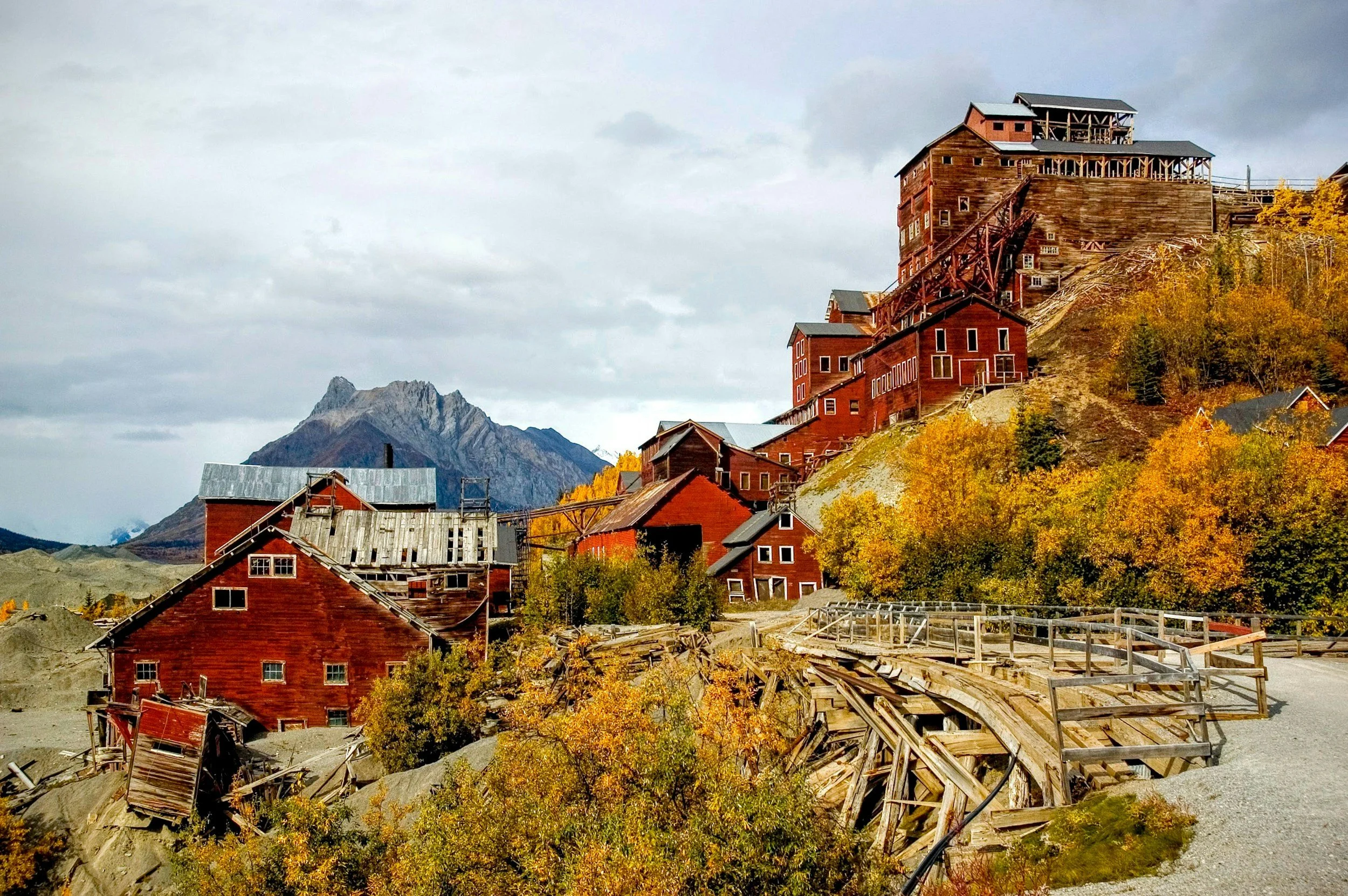 Old red wooden buildings on a hillside with a mountain in the background and autumn trees in the foreground.