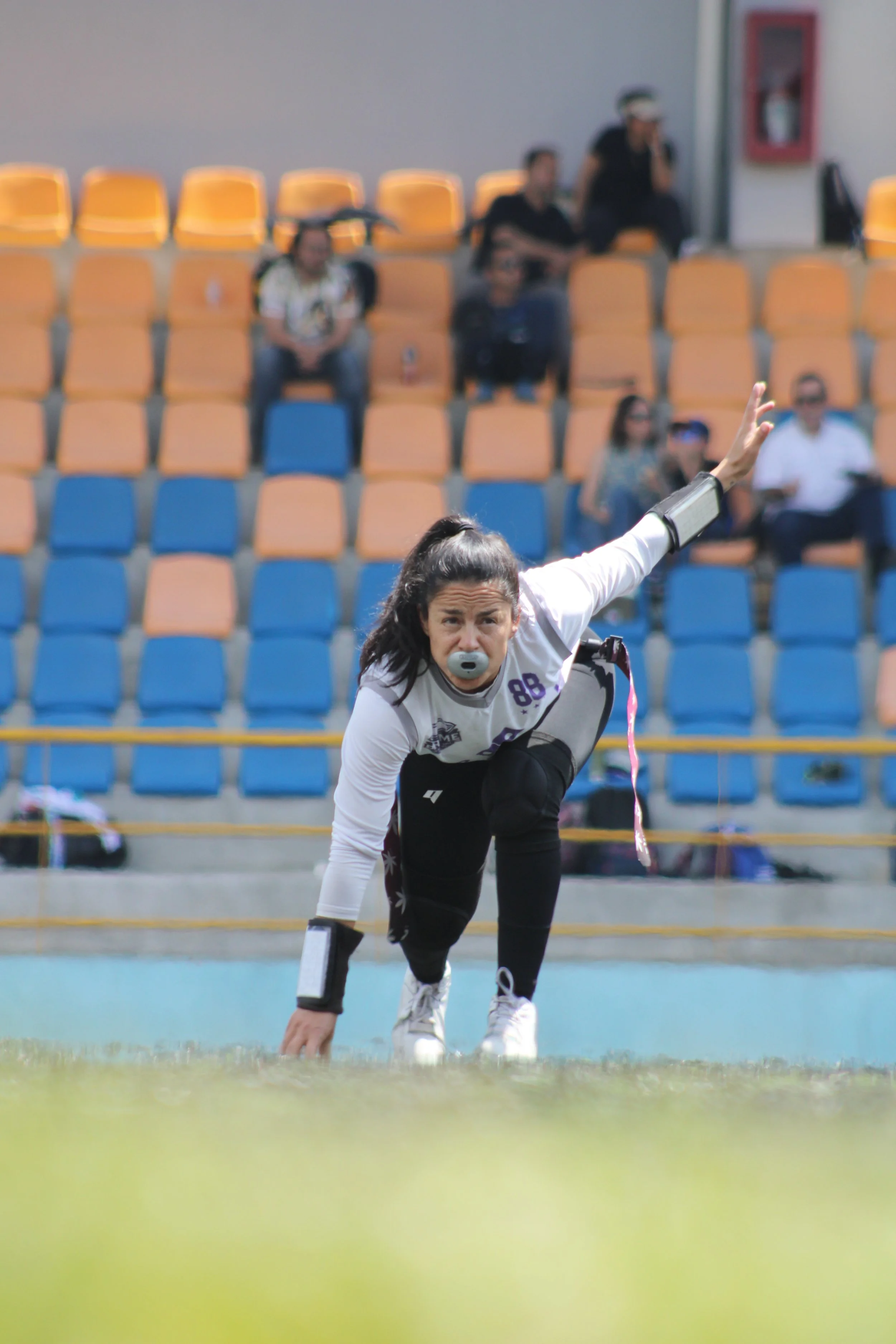 A female athlete in sports gear preparing for a race on a track, with spectators seated in the background.