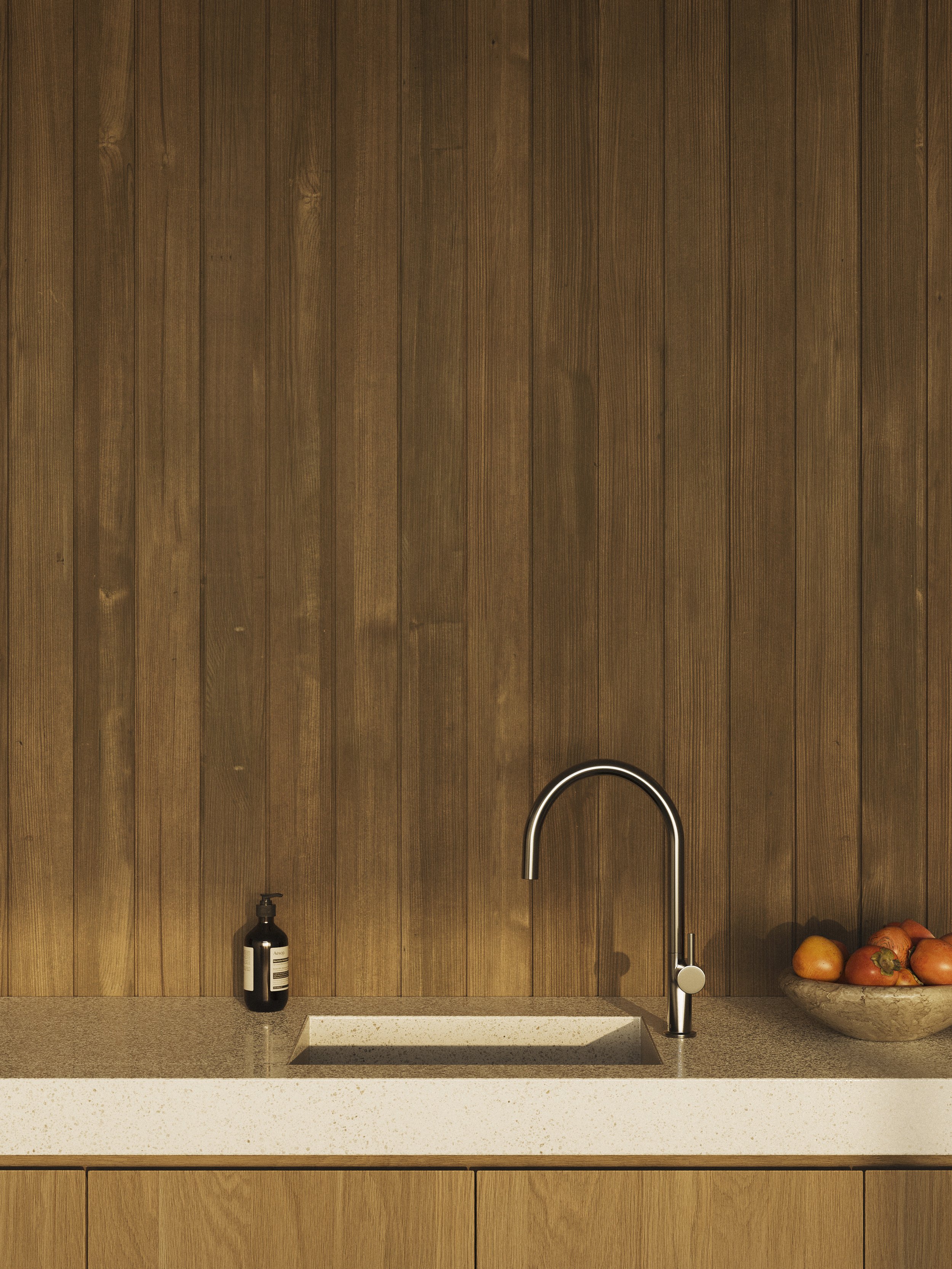 Kitchen with wooden wall paneling, a beige speckled countertop, a stainless steel faucet over a sink, a black soap dispenser, and a wooden bowl of oranges and tomatoes.