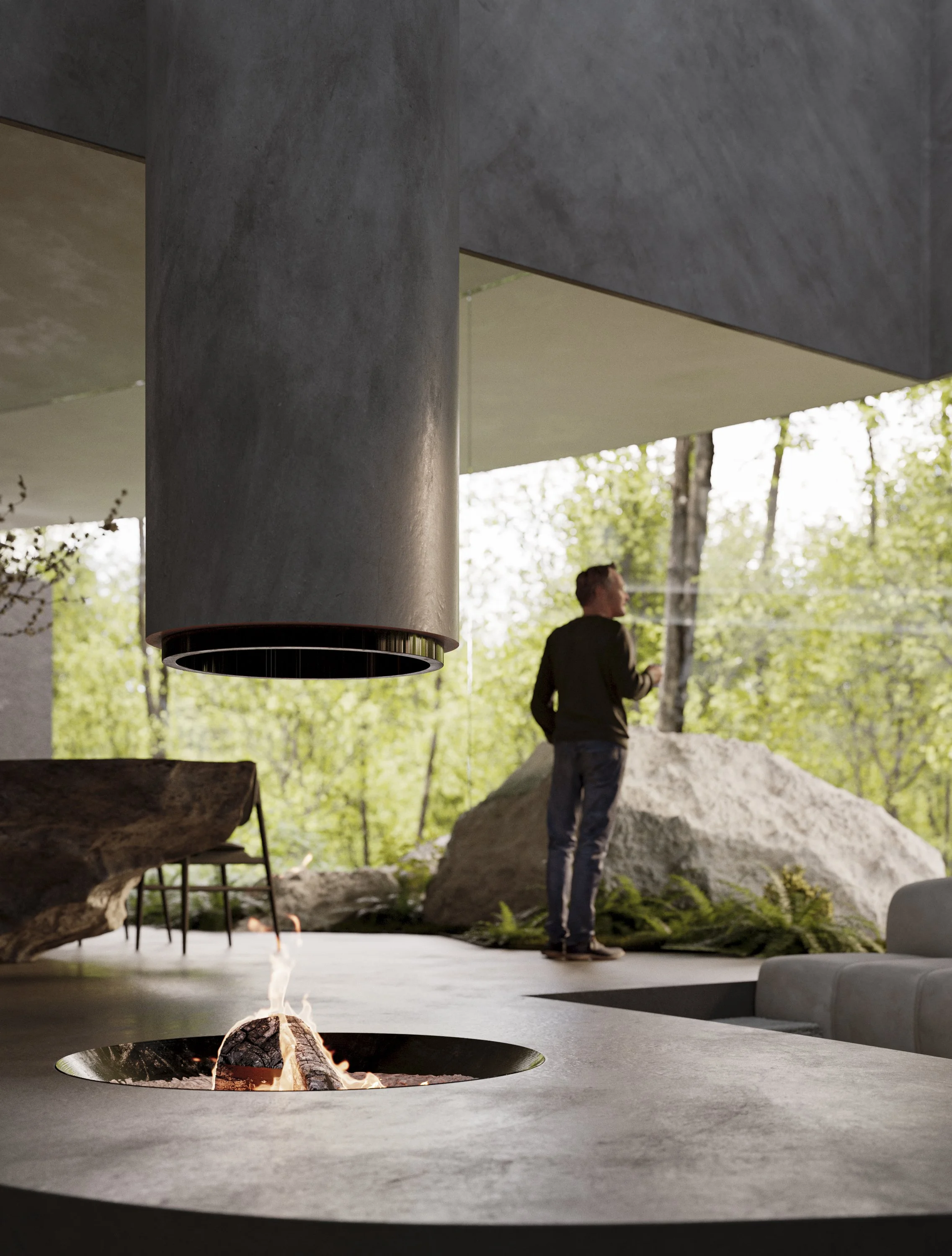 Interior view of a modern house with a fire pit, a large gray hanging chimney, and a person standing outside amidst trees and rocks.